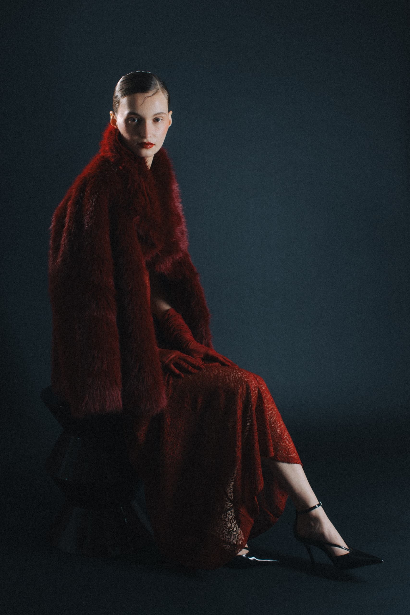 Elegant woman in a luxurious red fur coat and dress sitting stylishly.