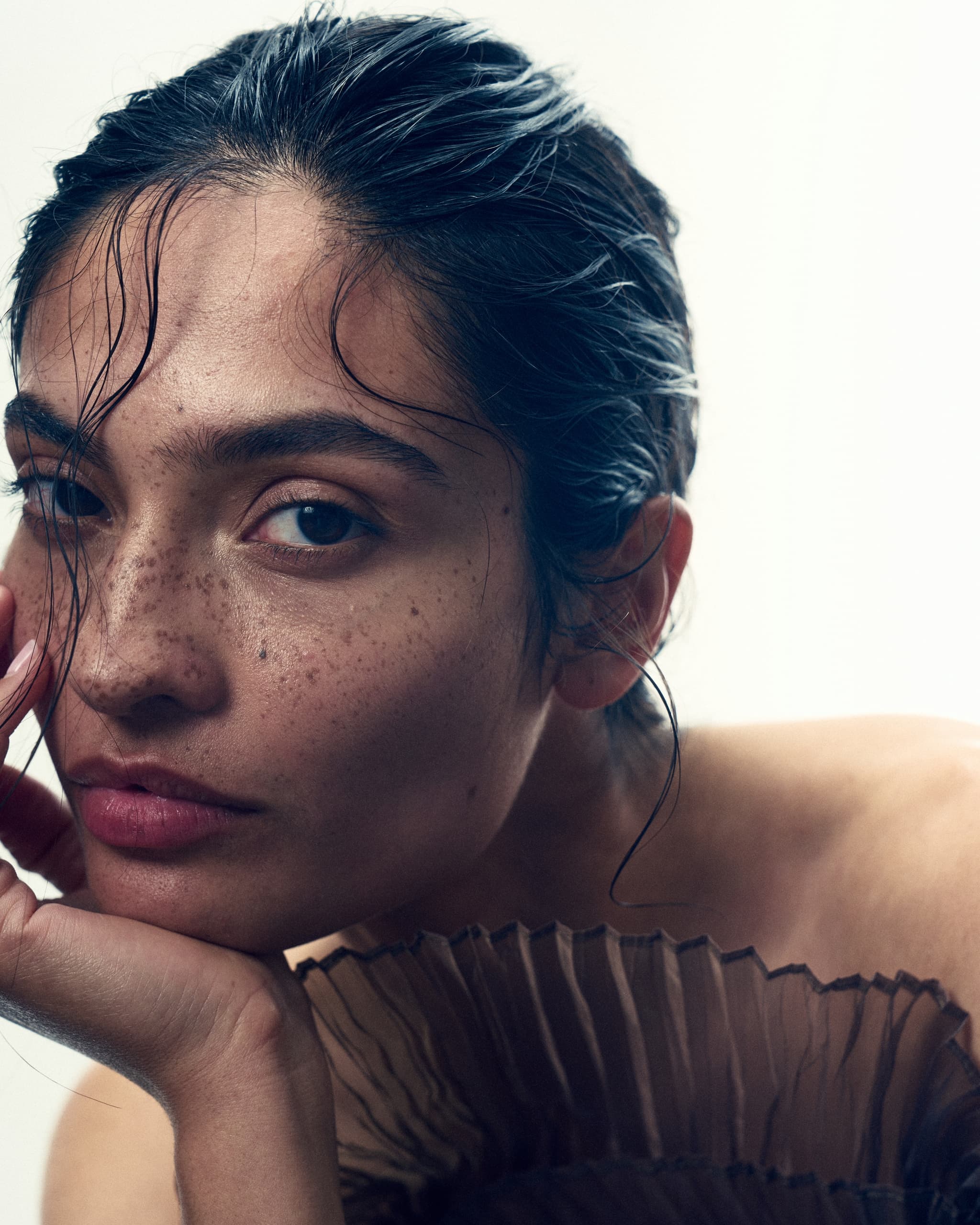 Close-up of a serene woman with freckles and dark hair, wearing a textured garment.
