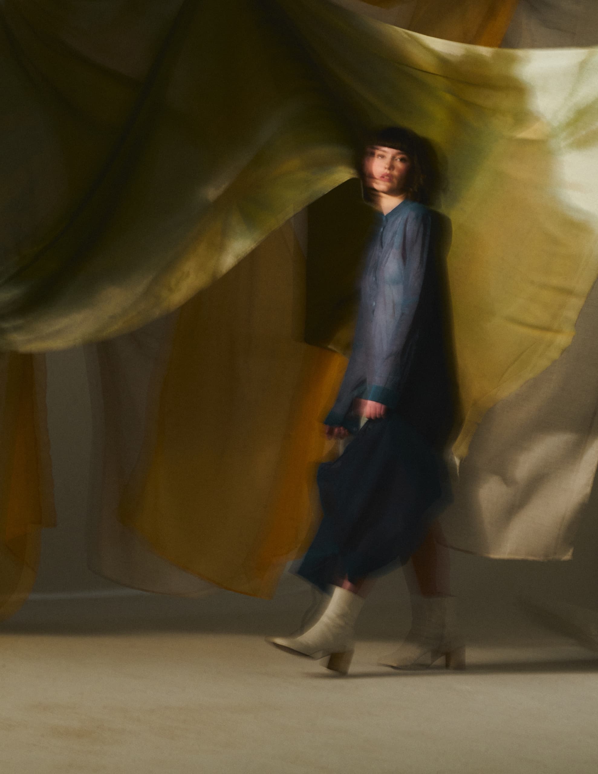 Blurred woman in flowing dress with layered fabric background.