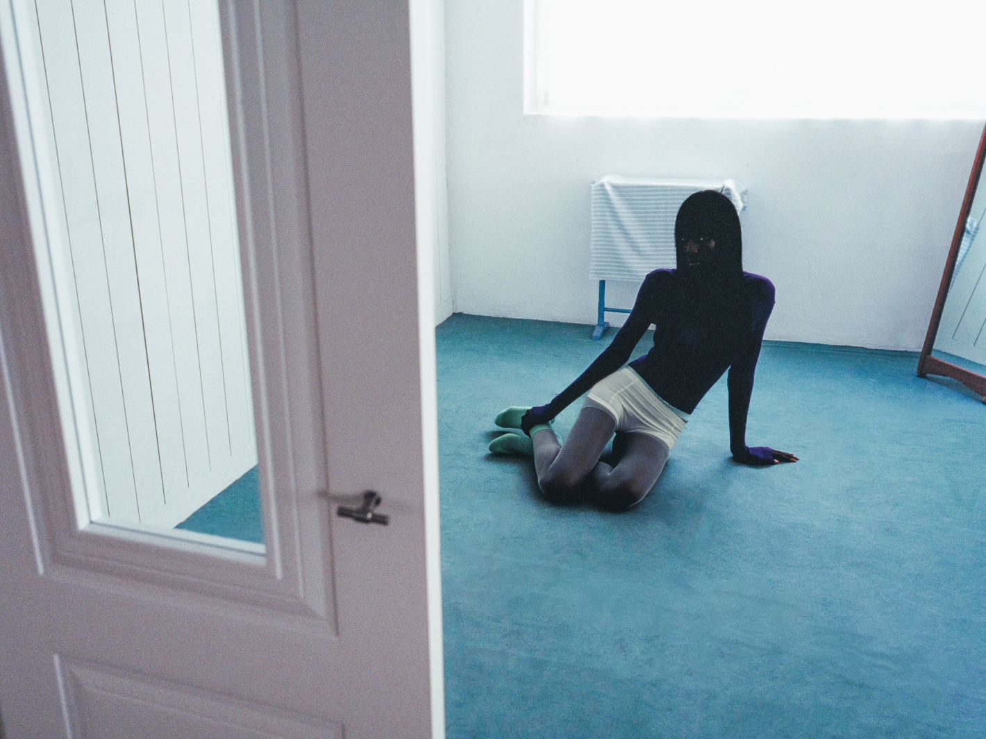 Person posing in a minimalist room with blue floor and white walls.