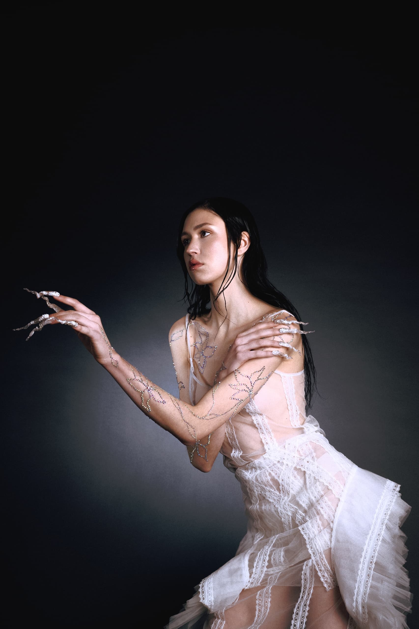 Woman in a creative lace dress with artistic makeup and pose, dark background.