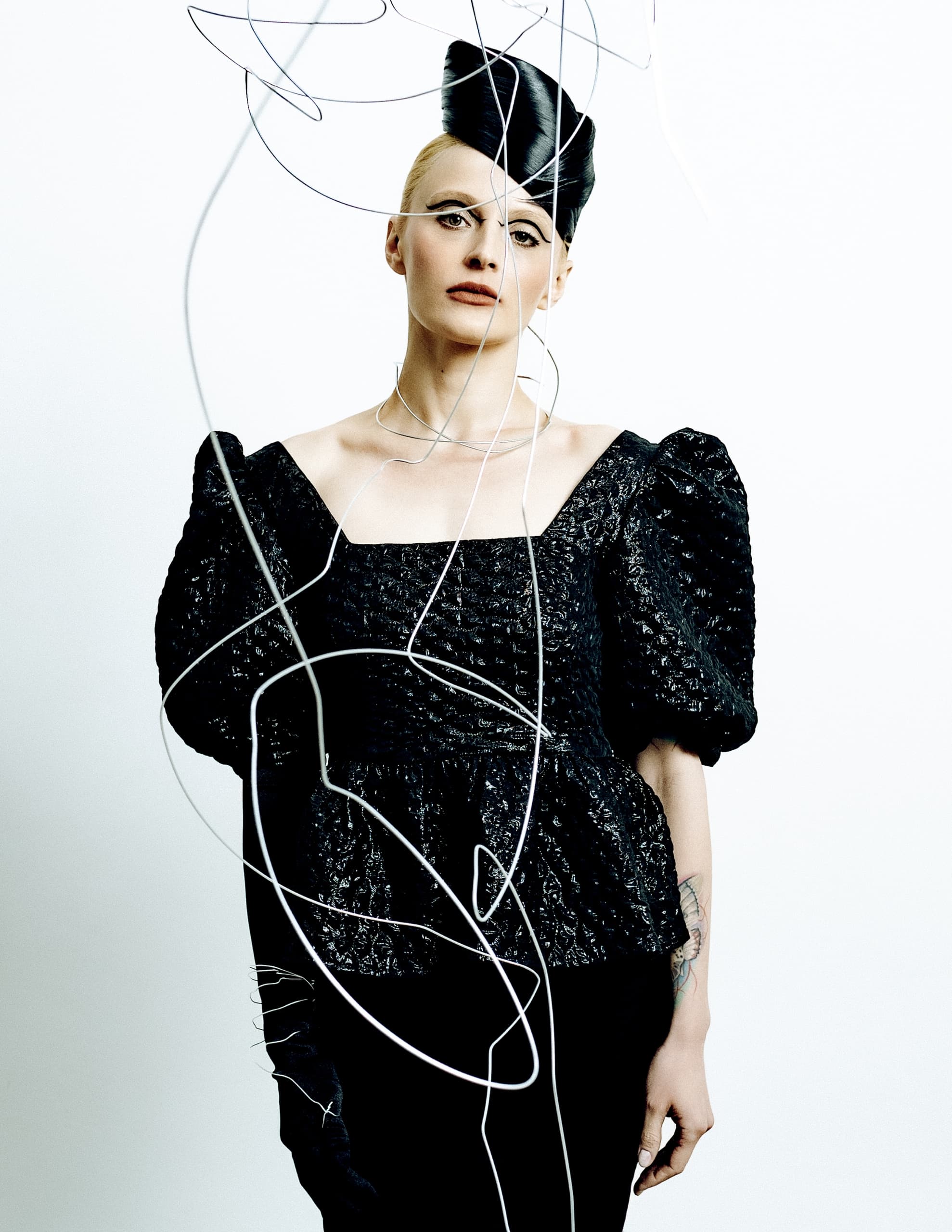 Avant-garde fashion model in structured black dress with unique hairstyle and wires.