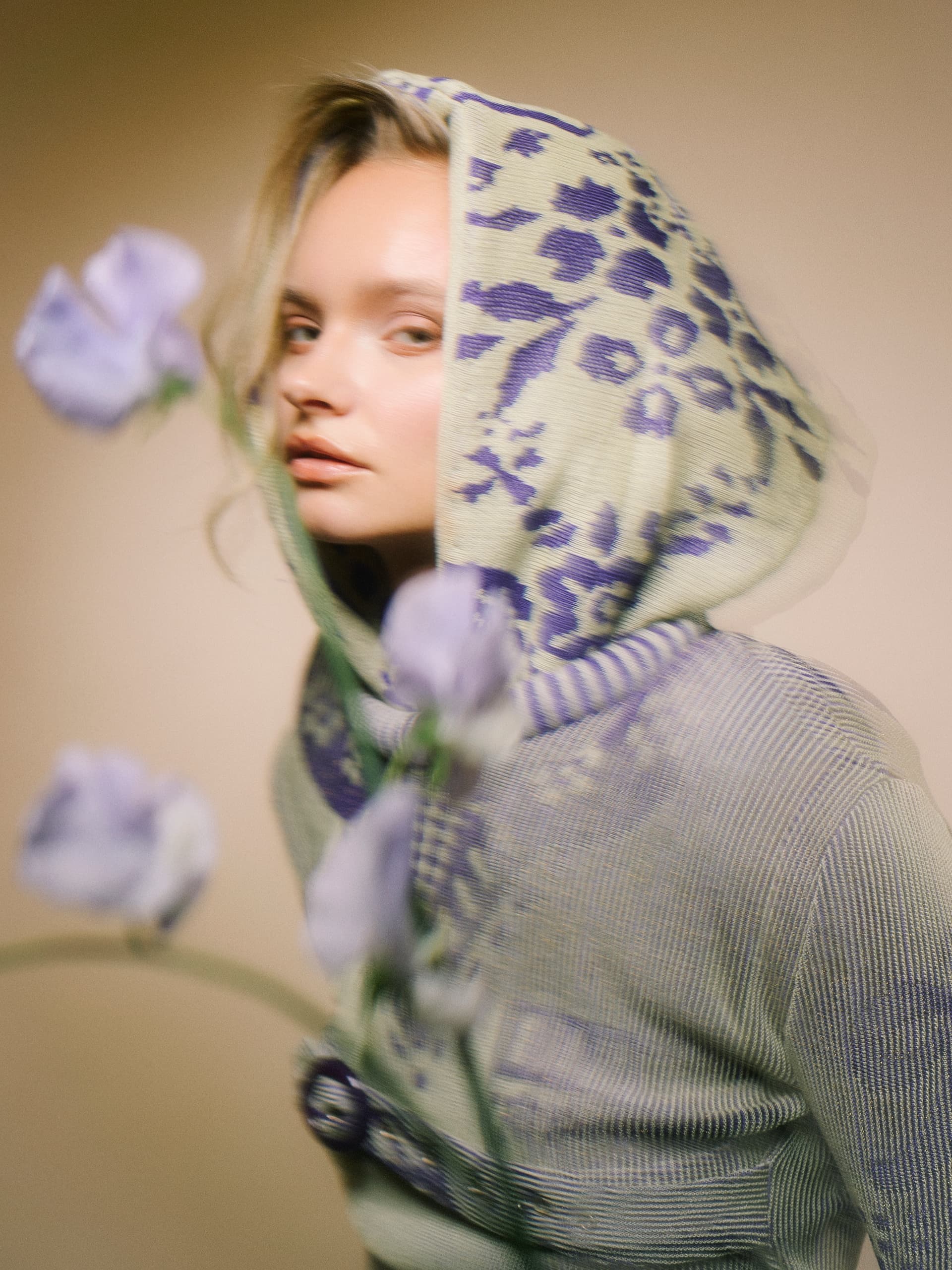 Blurry model in patterned hoodie with flowers in foreground.