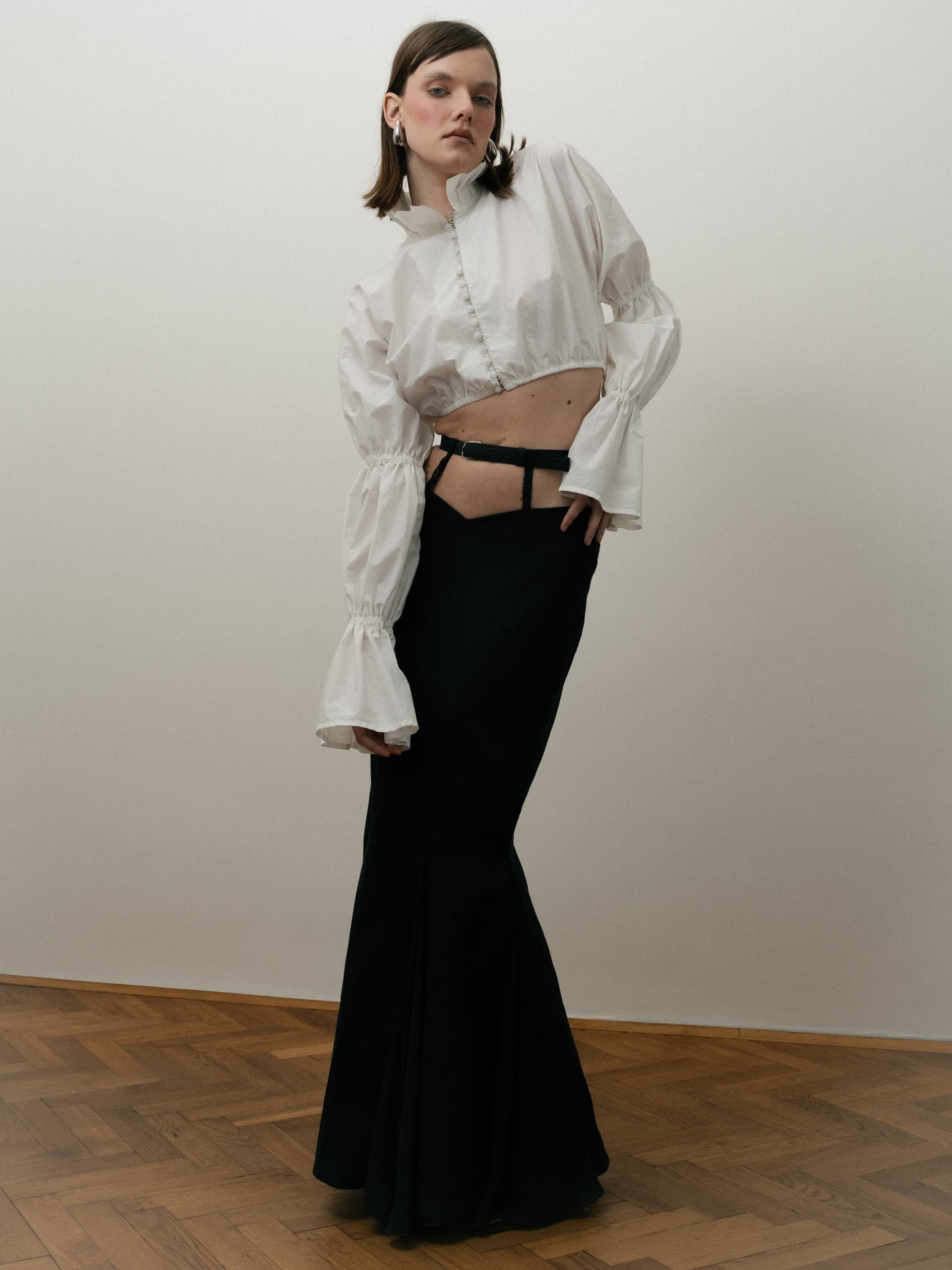 Fashionable woman in chic white blouse and black skirt posing indoors on wood floor