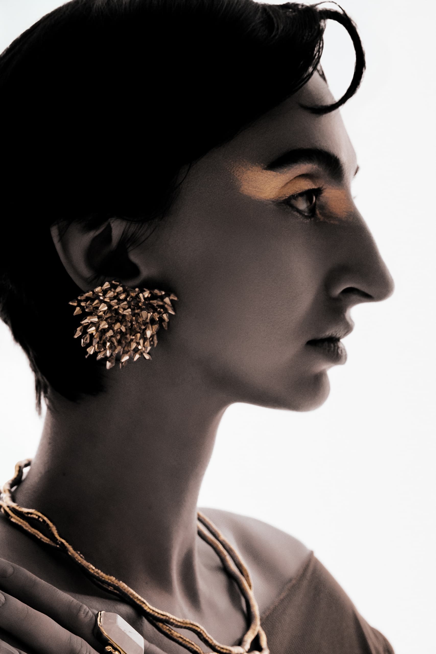 Elegant woman with gold earrings and makeup, artistic black and white portrait.