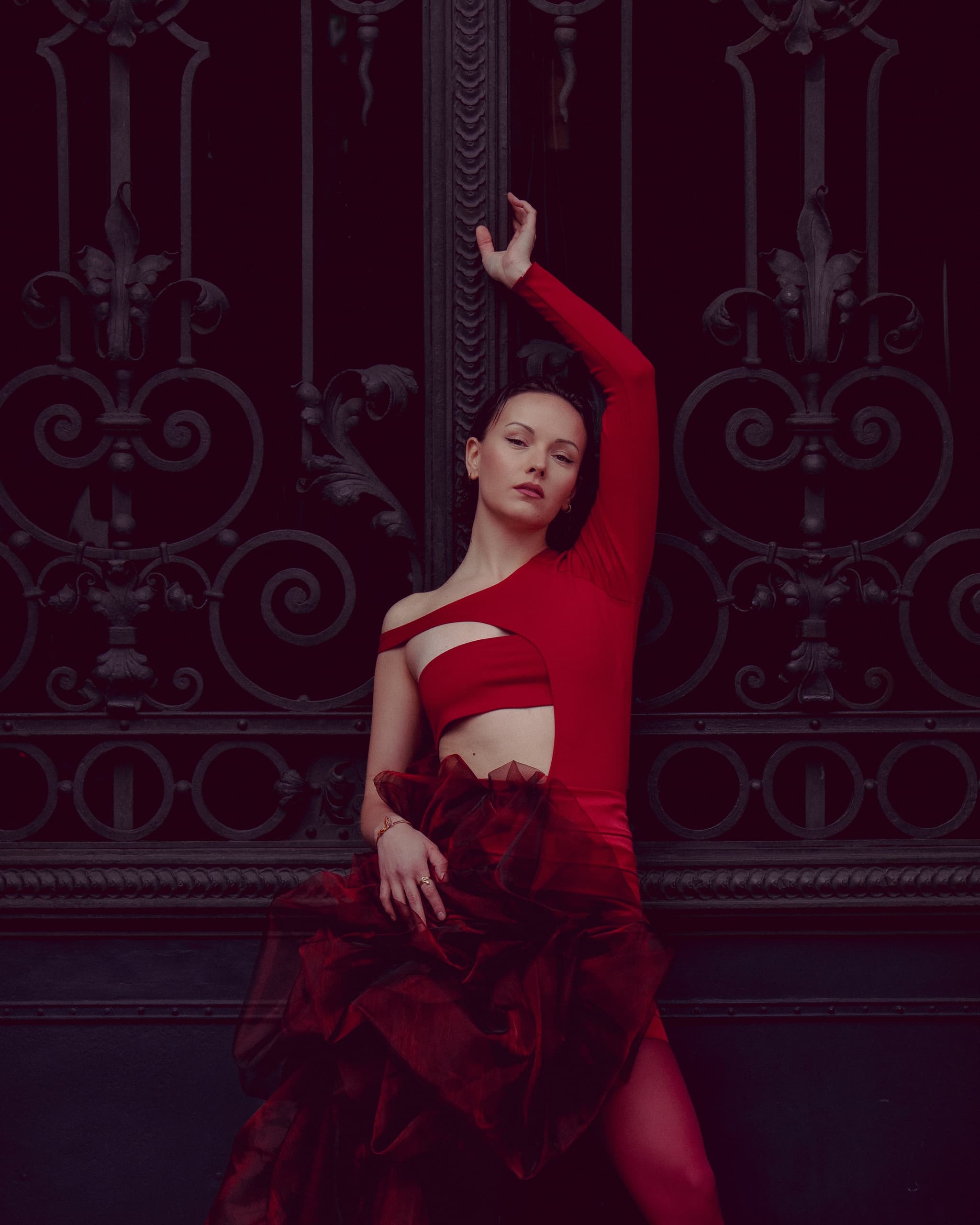 Woman in elegant red dress posing by ornate metal gate.