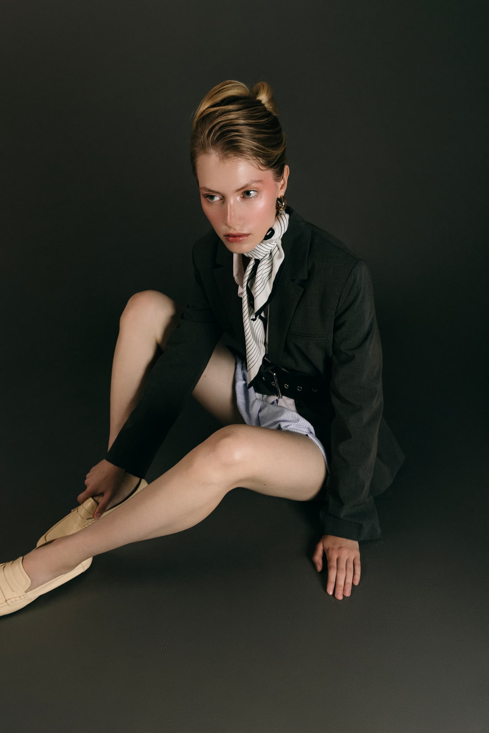 Fashionable woman poses in a blazer and scarf on dark background.
