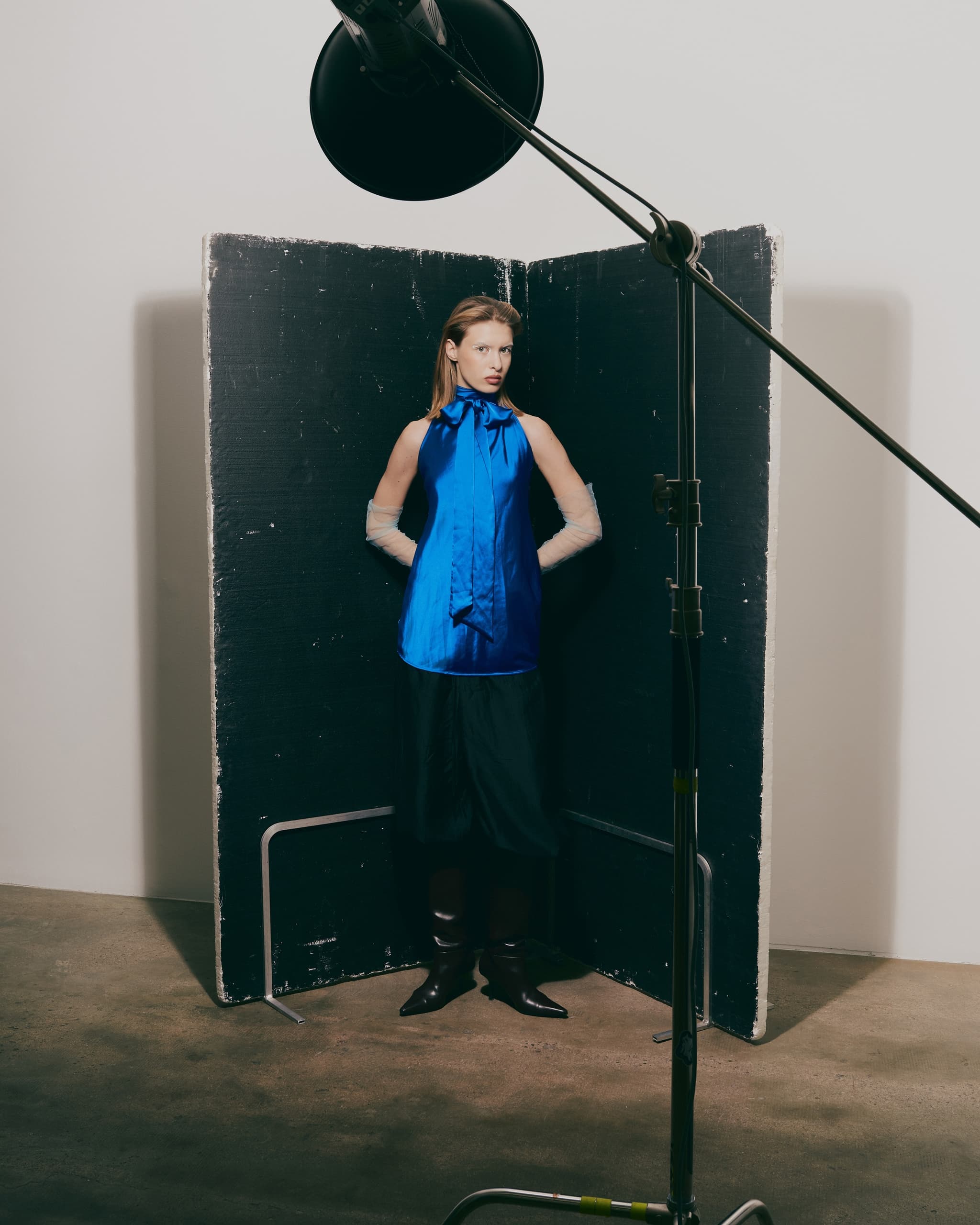 Model poses in blue top, black skirt, in a professional photo shoot setup.