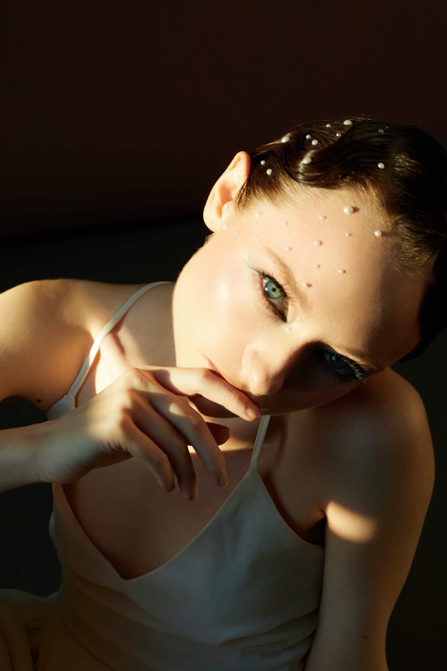 Woman with pearl-decorated face and intense gaze in soft lighting.