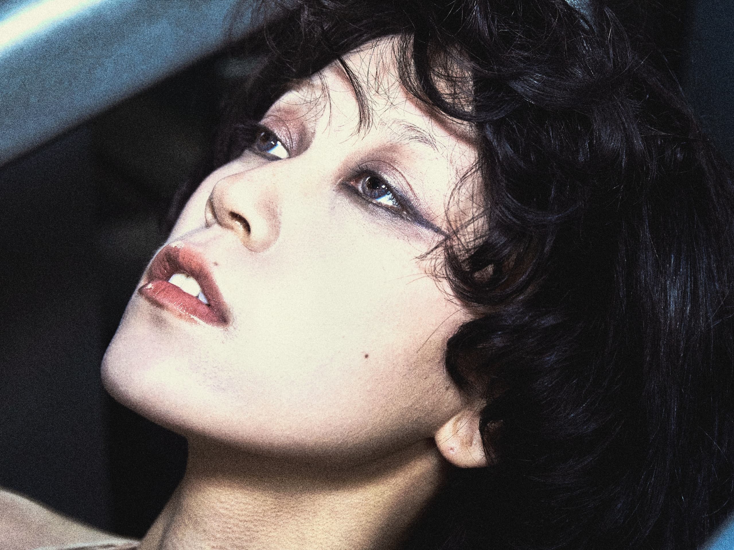 Person with thoughtful expression and dark hair in soft lighting.