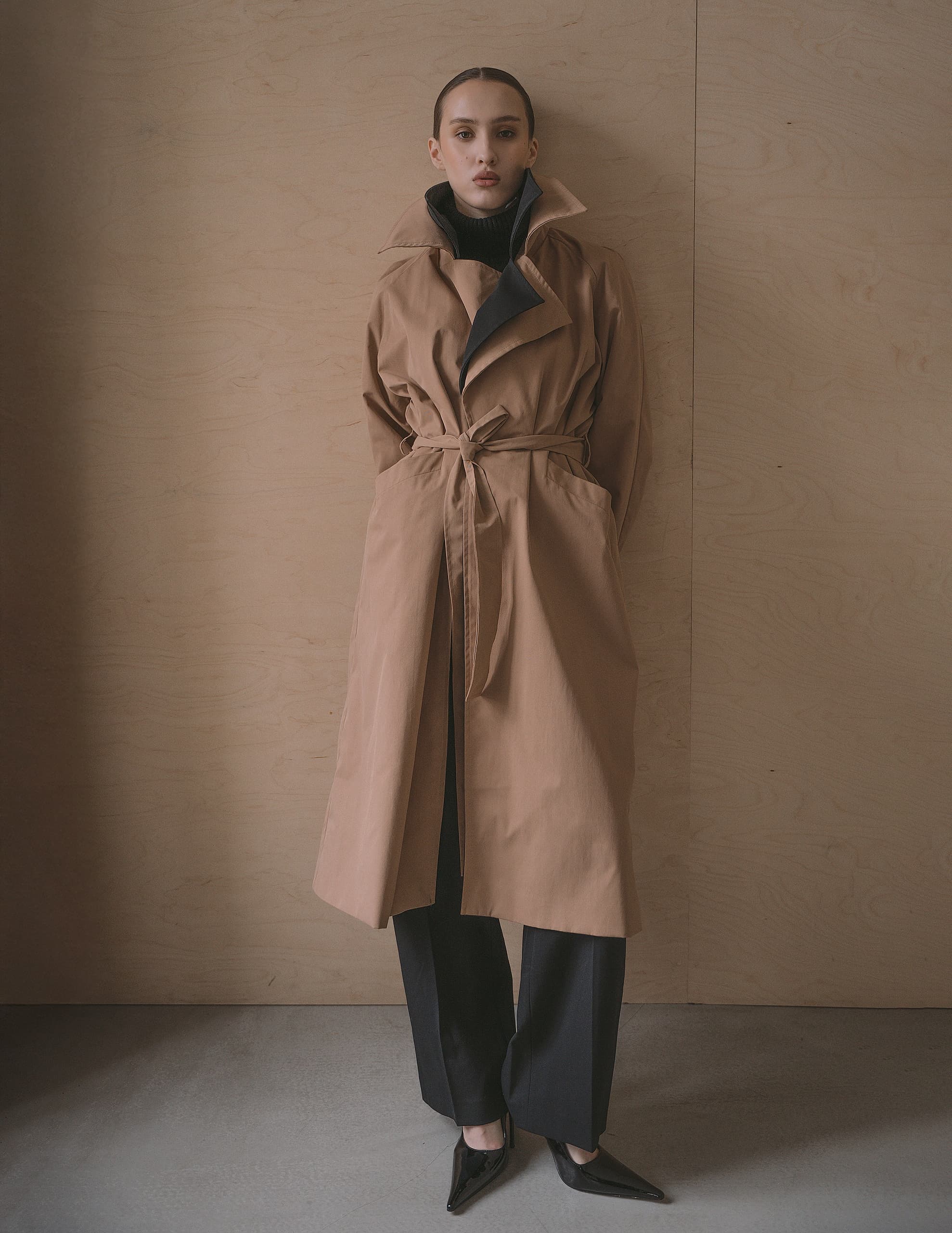 Fashionable woman in a tan trench coat against a wooden background.