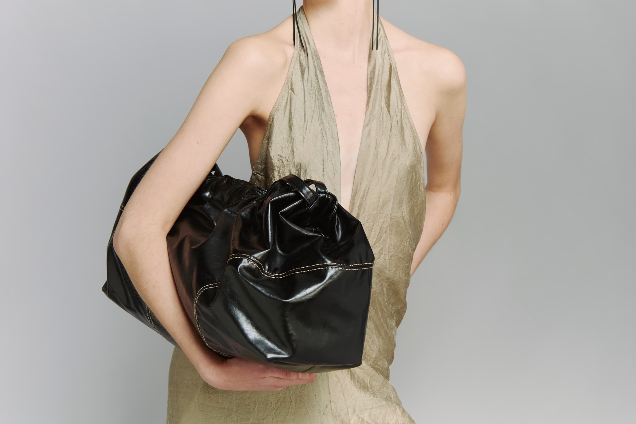 Stylish woman holding a large black leather bag in a beige dress.