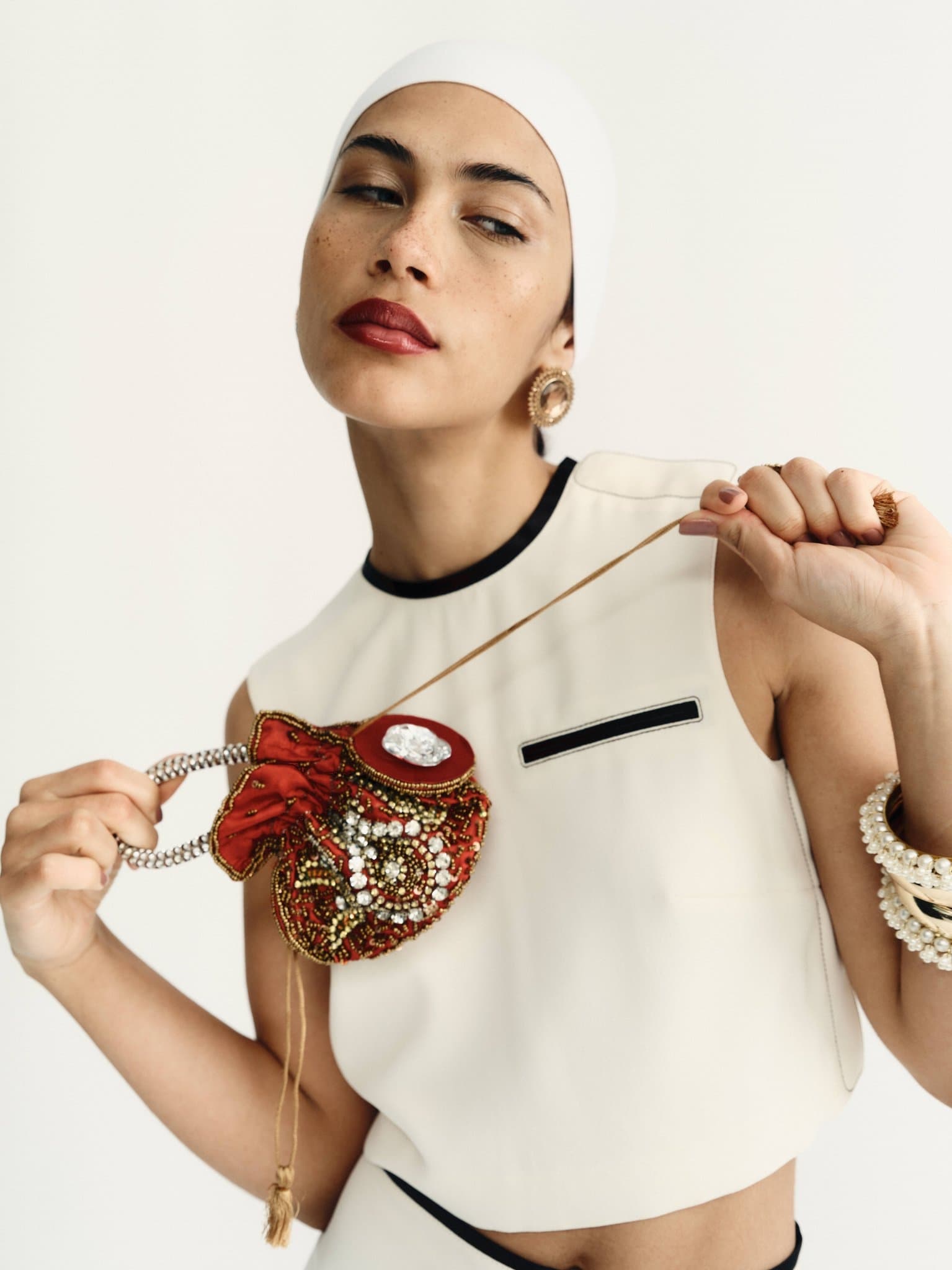 Fashionable woman with pearl accessories holding an ornate red beaded pouch.