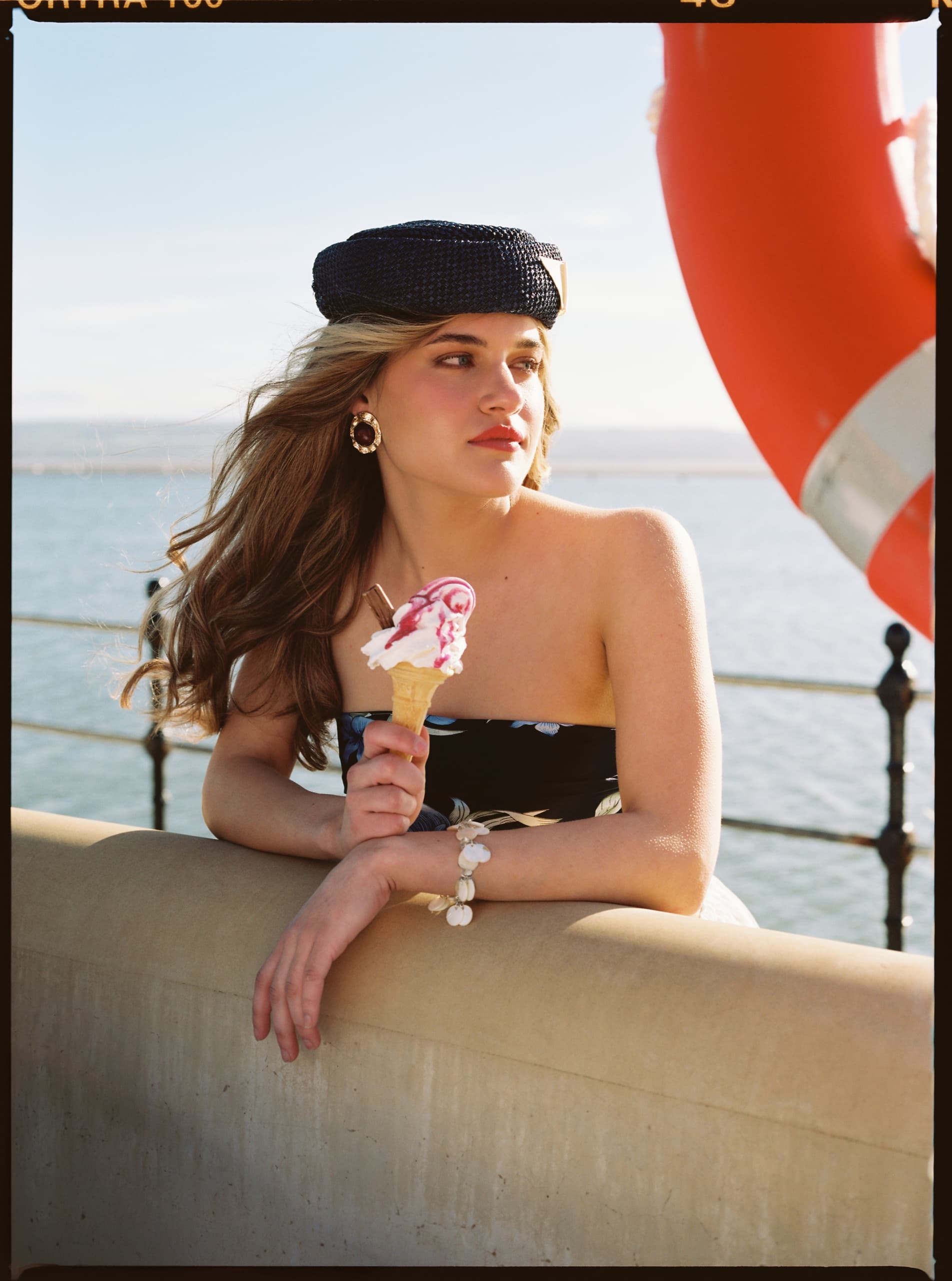 Woman enjoying ice cream by the seaside, wearing a stylish hat and summer dress.