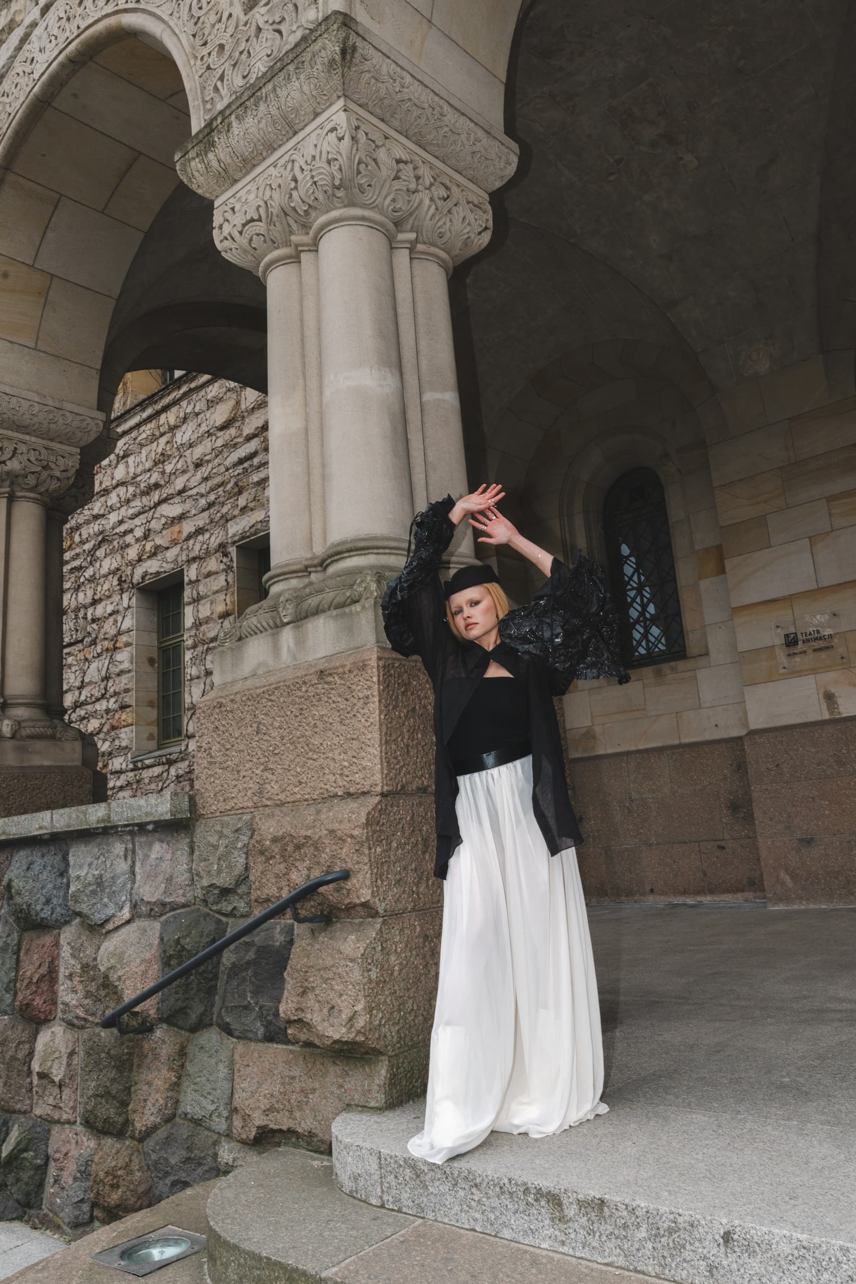 Woman in stylish outfit posing by ornate stone arches.