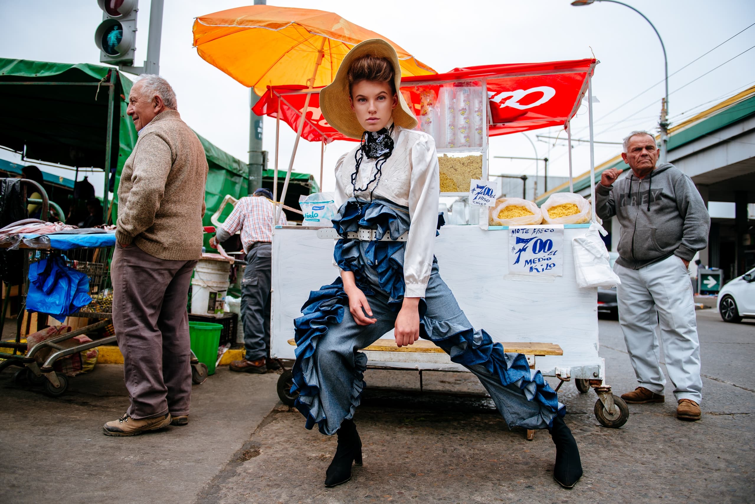 Fashionable model posing at vibrant outdoor market under colorful umbrellas.