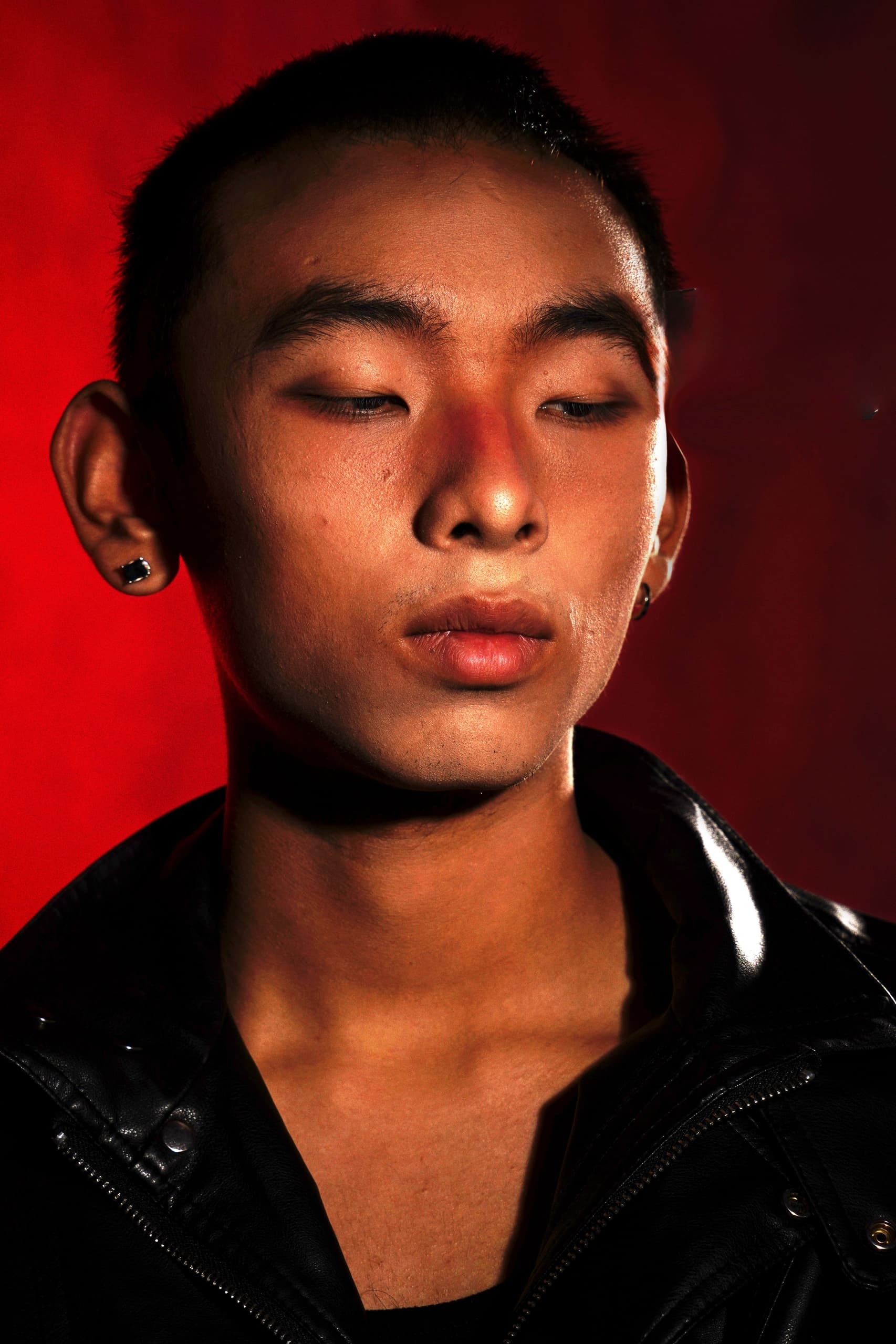 Portrait of a person in a leather jacket, against a vibrant red background.