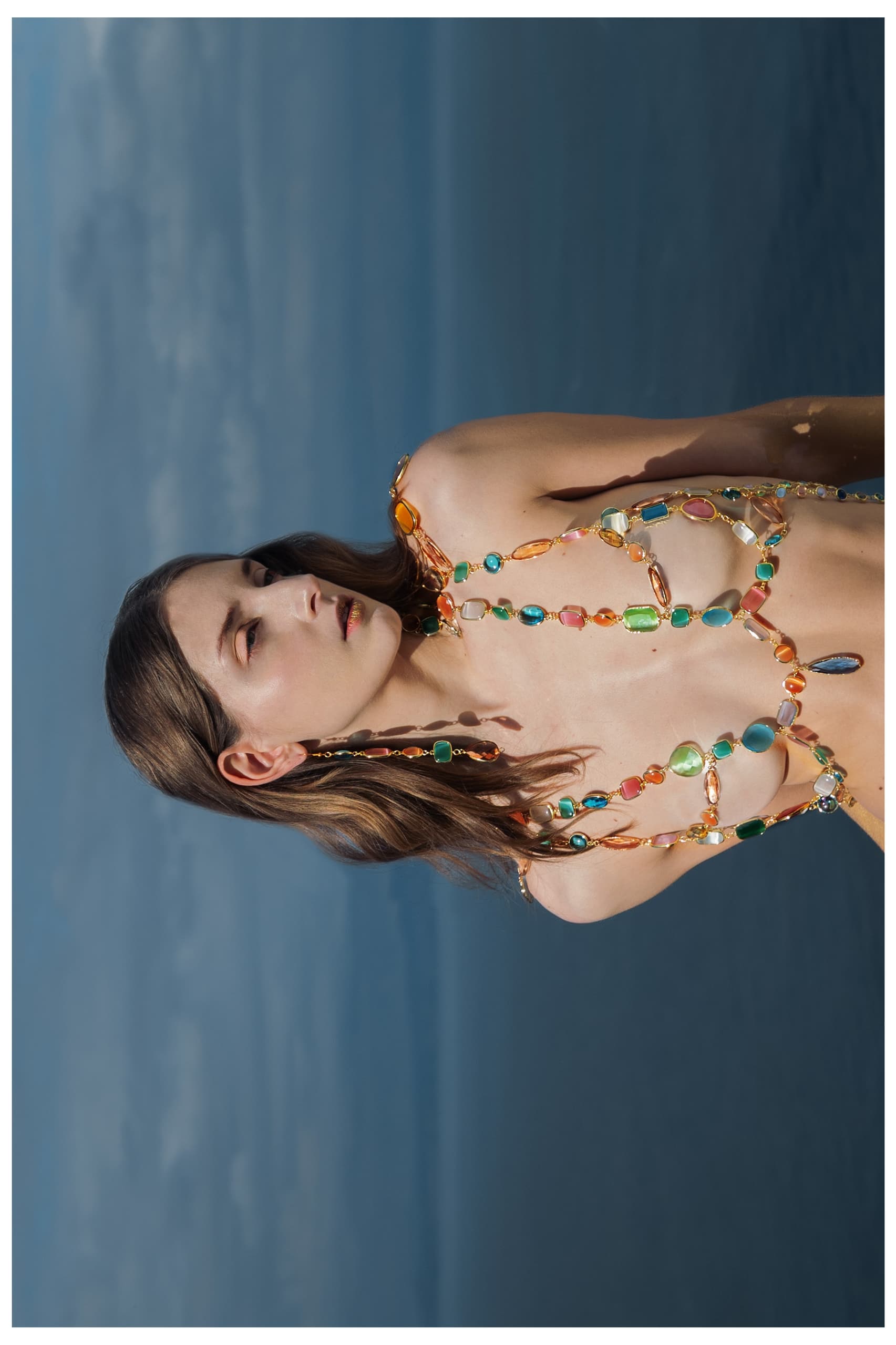Model adorned in colorful gemstones with ocean backdrop.