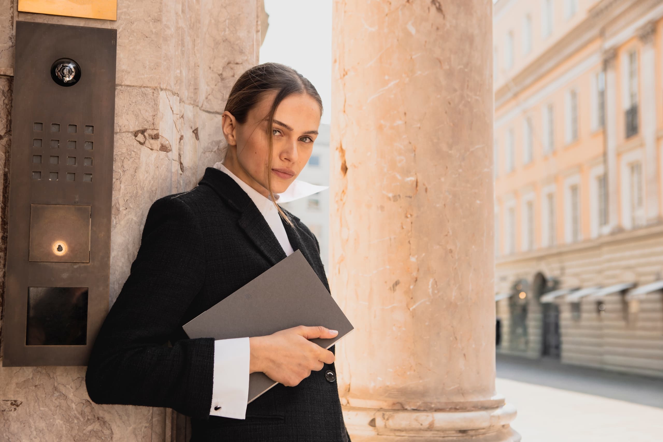 Businesswoman in formal attire holds a folder in urban setting.