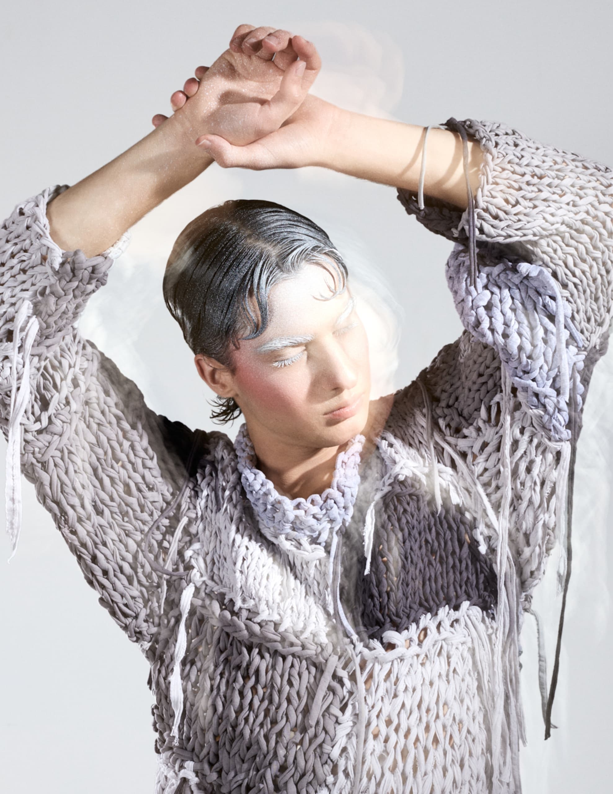 Person in artistic, textured outfit poses with arms raised in creative photography.