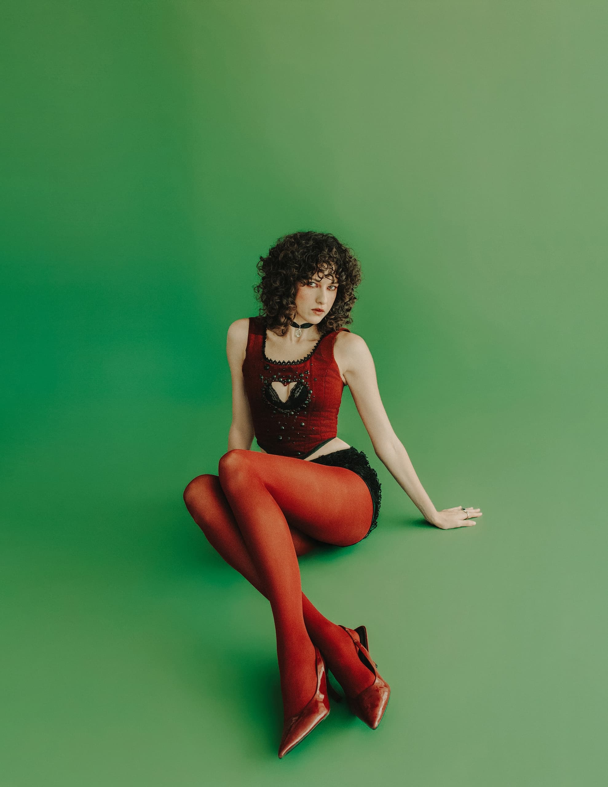 Person in elegant red outfit seated on green background.