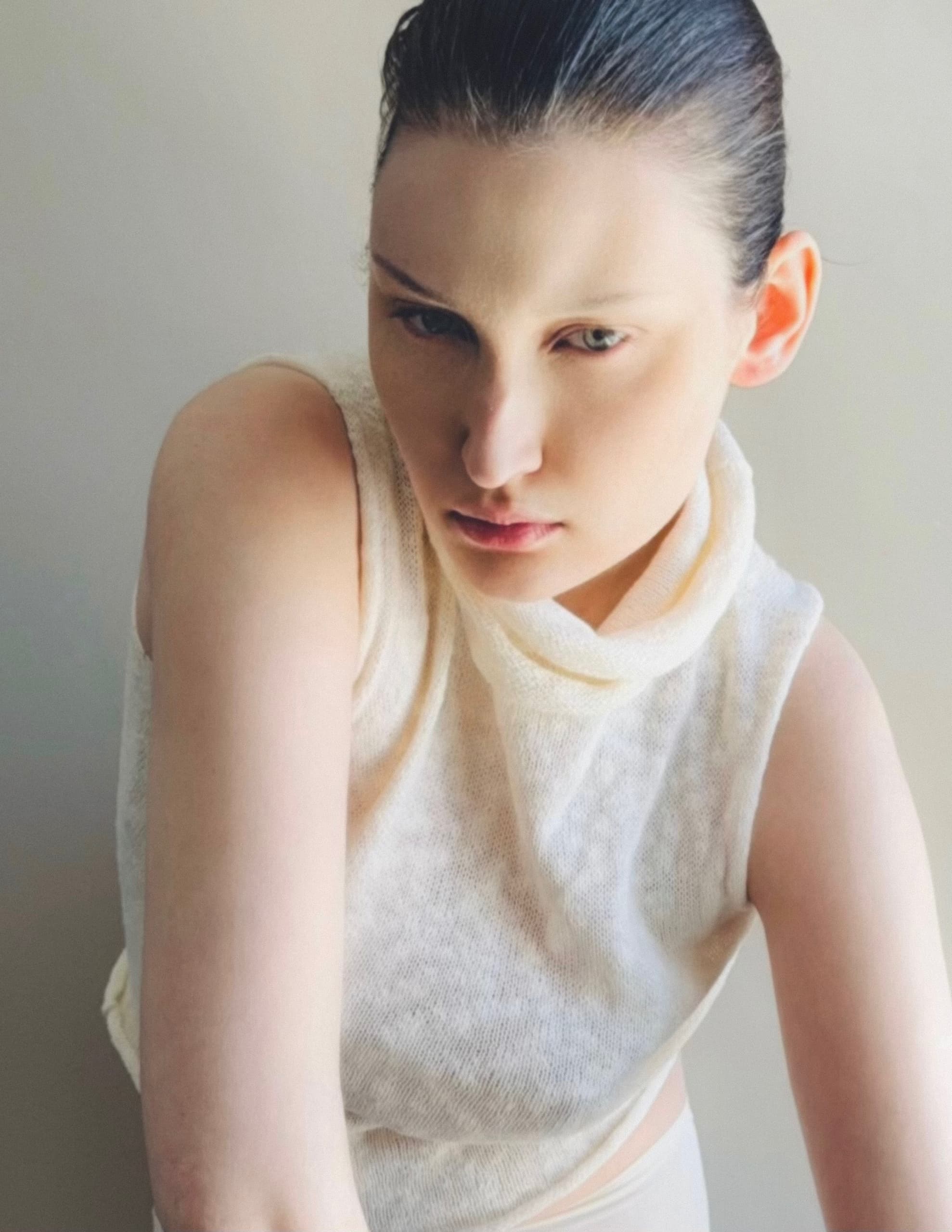 Elegant portrait of a model in a white sleeveless top, gazing thoughtfully.