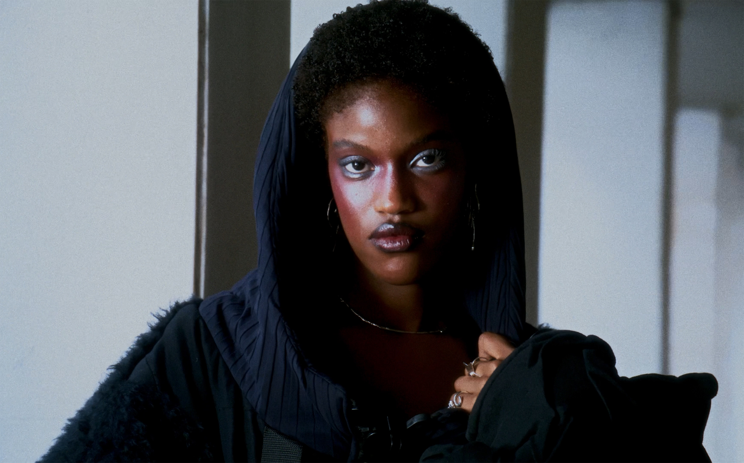 Person in stylish hooded outfit with bold makeup and confident expression.
