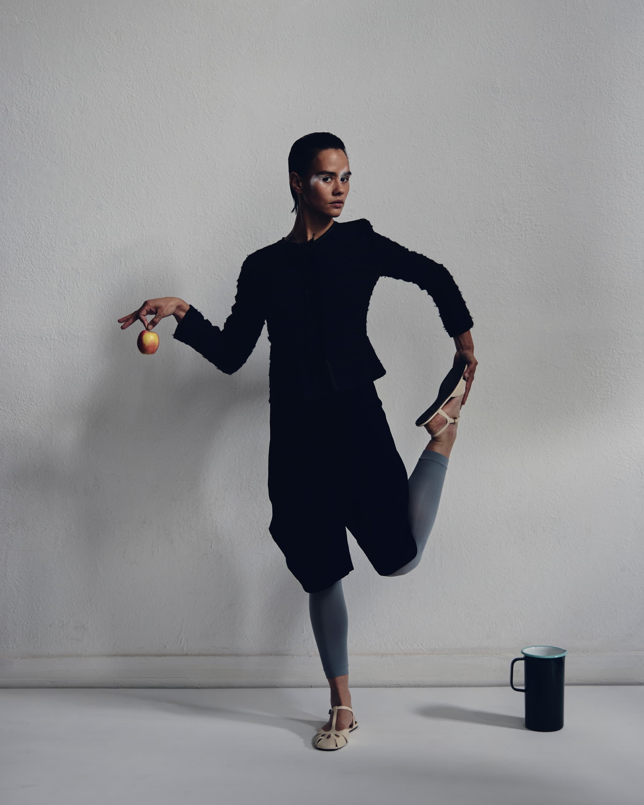 Fashion pose with apple and shoe, minimalist style against white background.