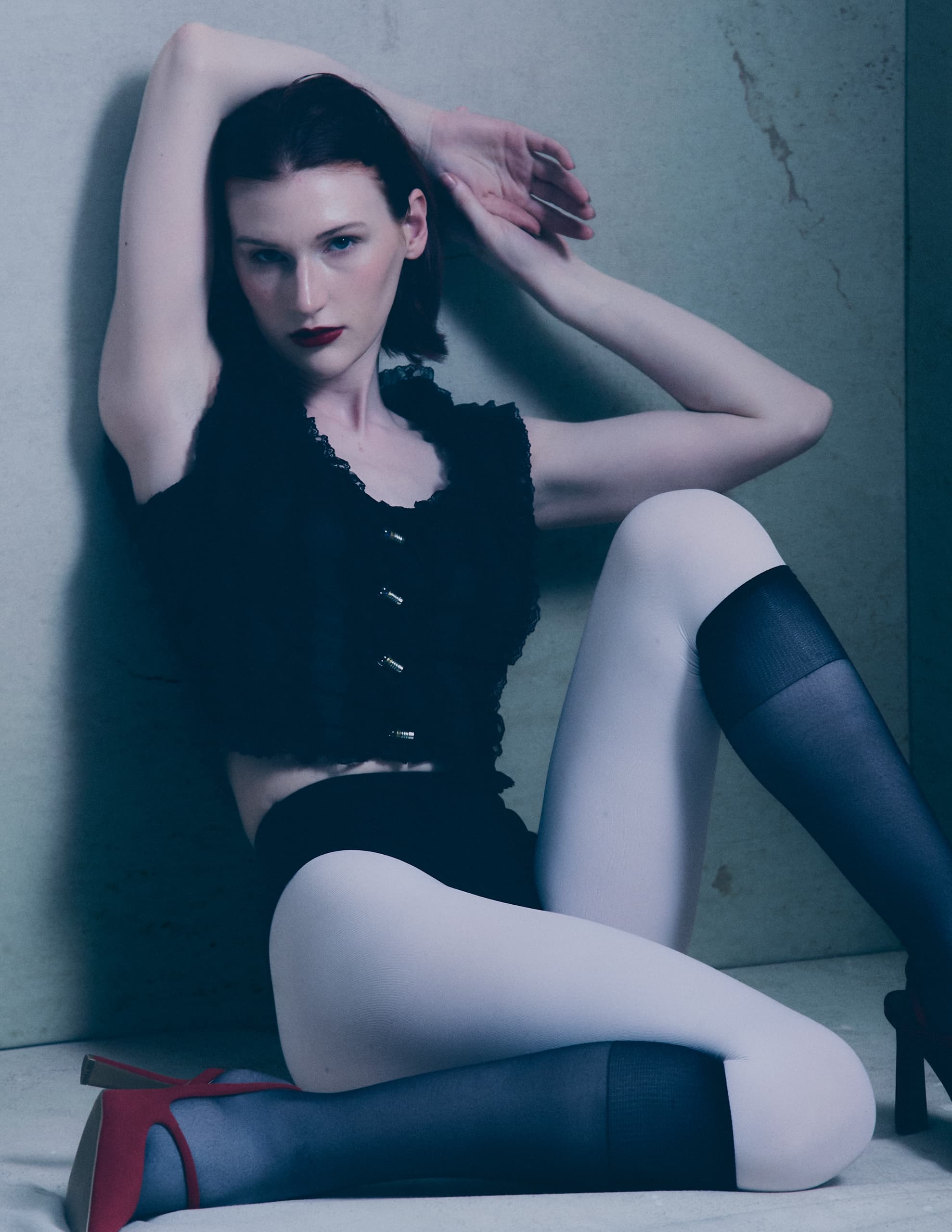 Stylish person poses in fashionable outfit with red heels and dark stockings.