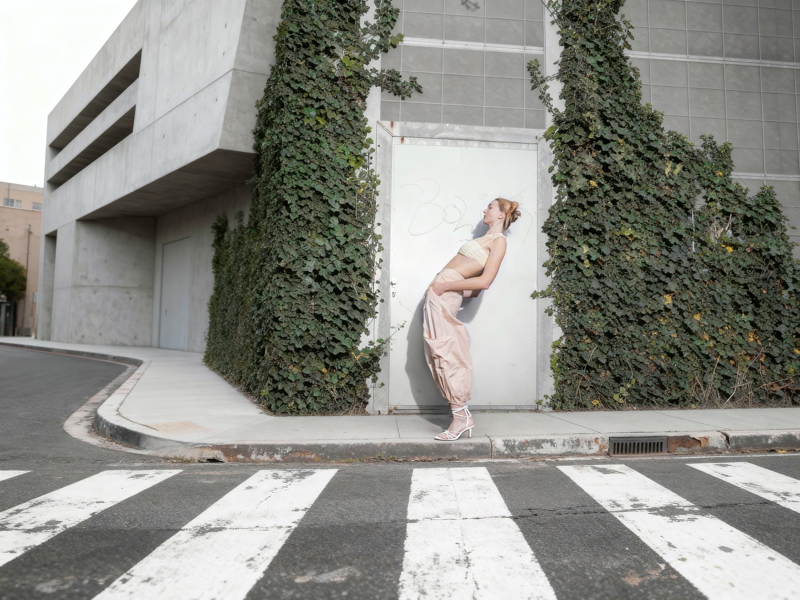 Stylish person in urban setting near ivy-covered wall and crosswalk.