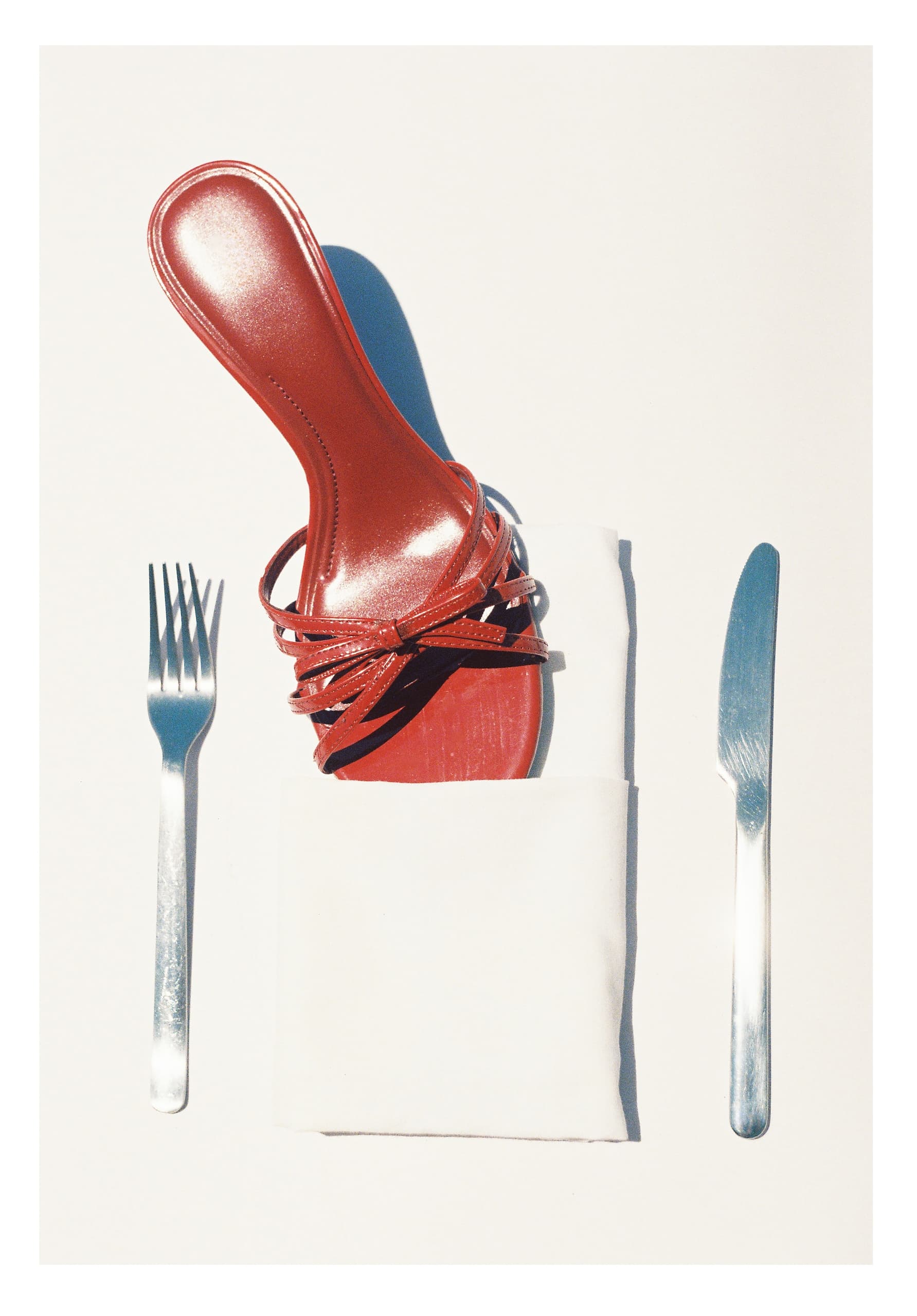 Red high heel on napkin between fork and knife, playful fashion concept.
