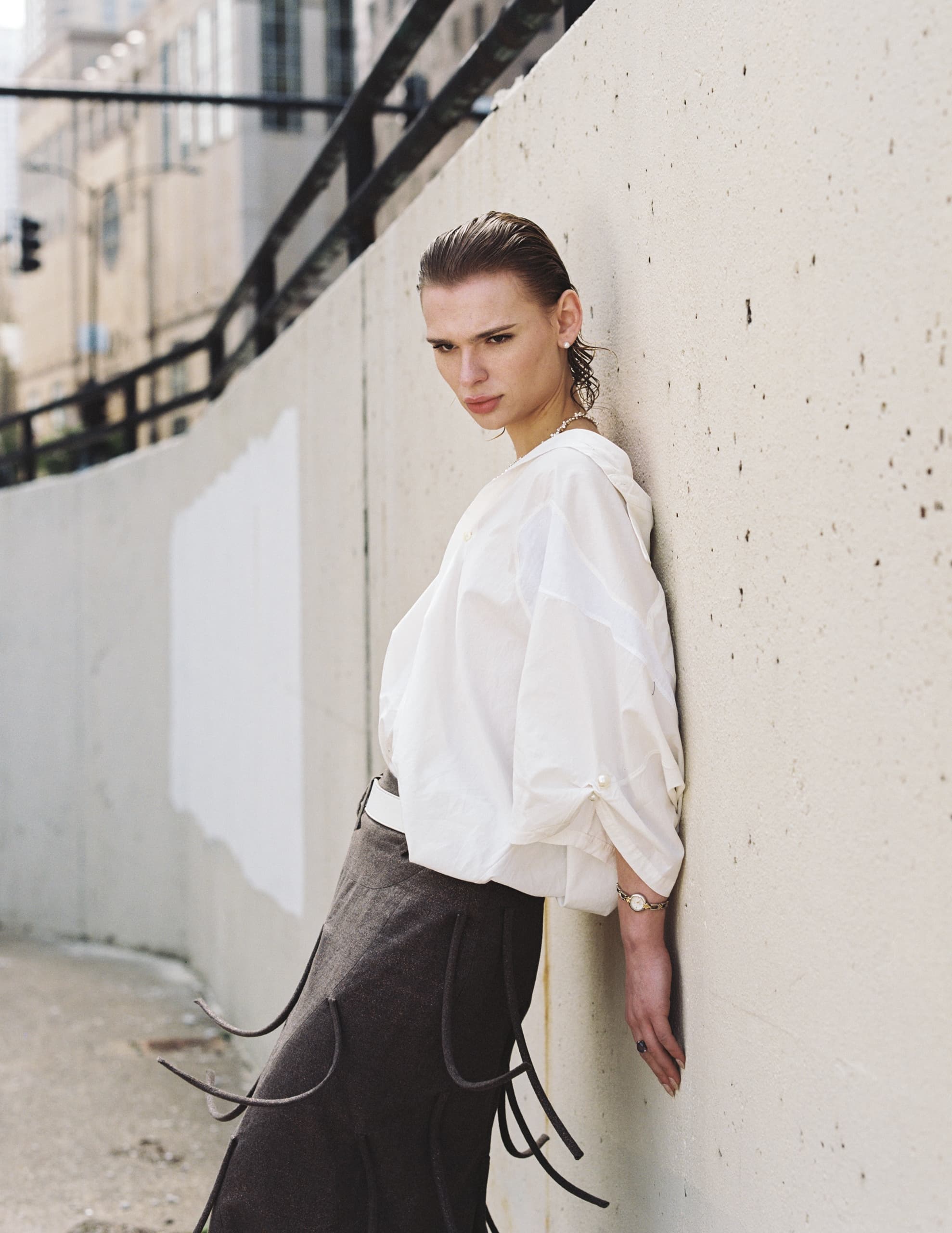 Person in stylish outfit leaning against a wall in an urban setting.