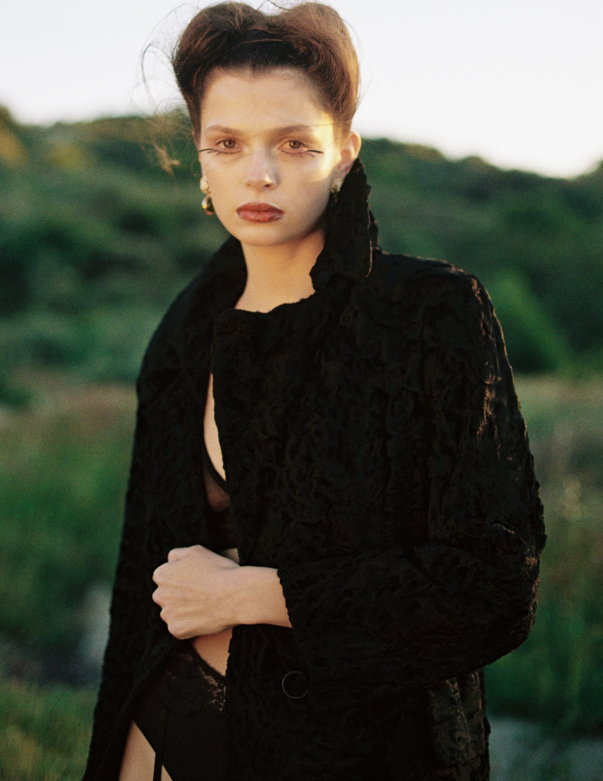 Fashion model in black coat posing outdoors at sunset.