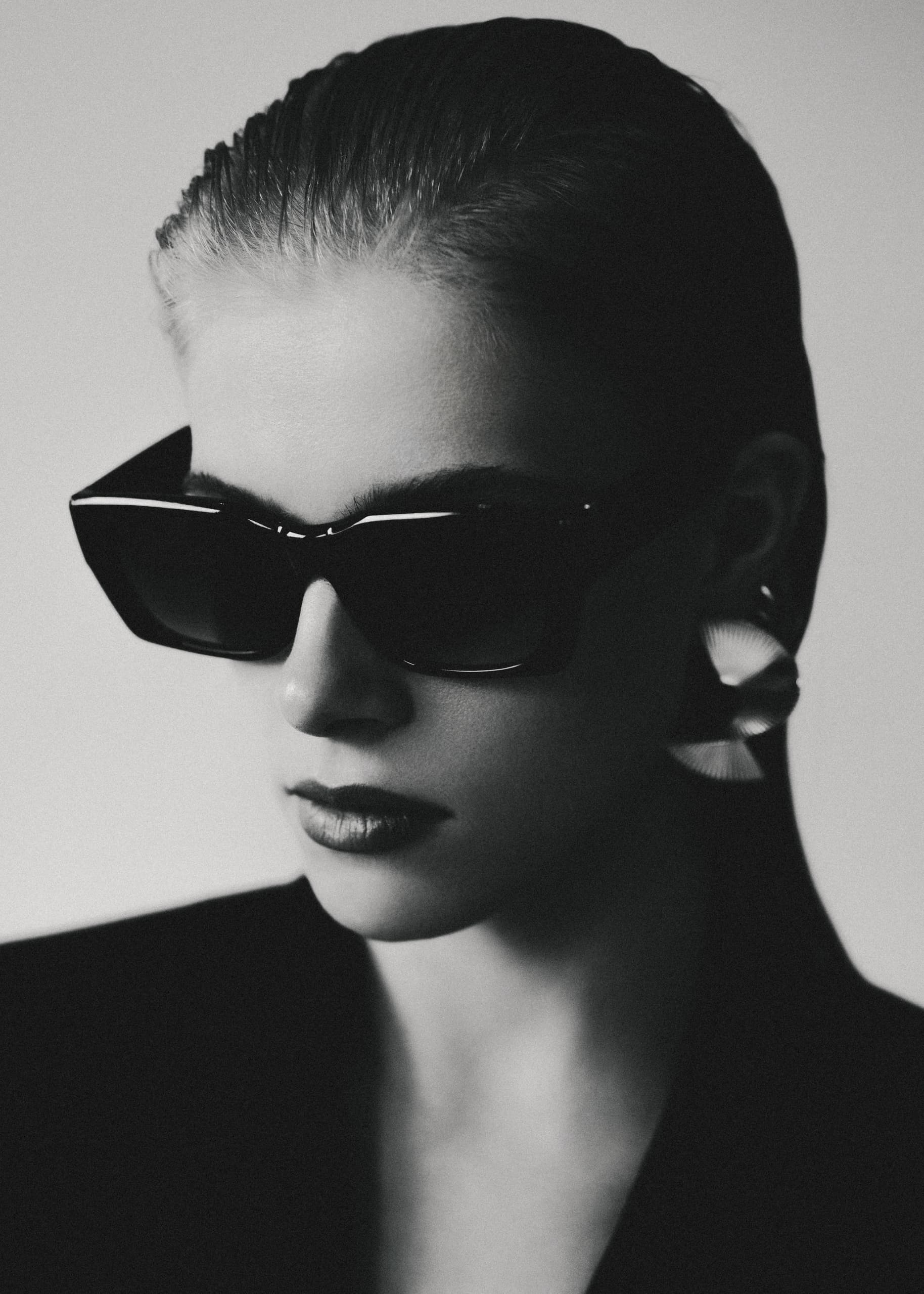 Stylish woman in sunglasses and earrings, black and white portrait.