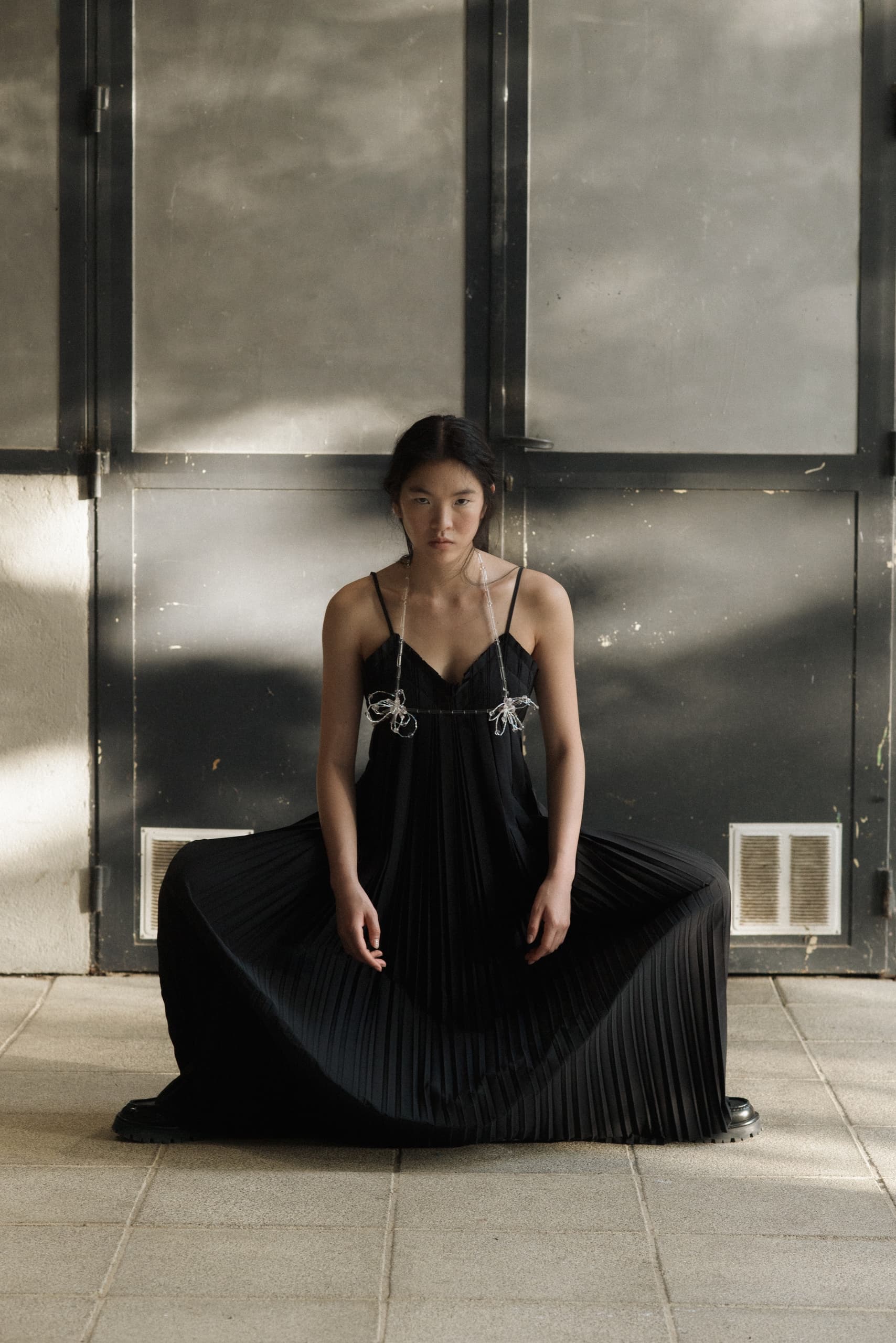 Person in pleated black dress sitting in front of a large industrial door.