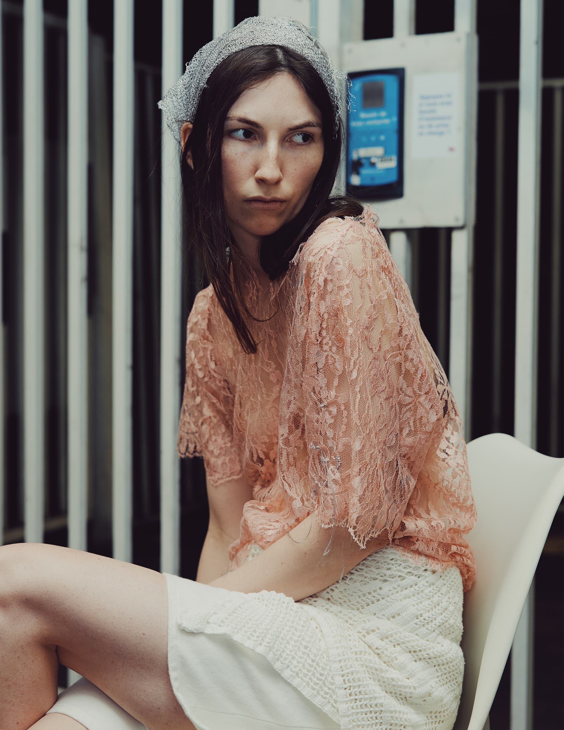 Woman wearing stylish lace top and headscarf, sitting indoors.