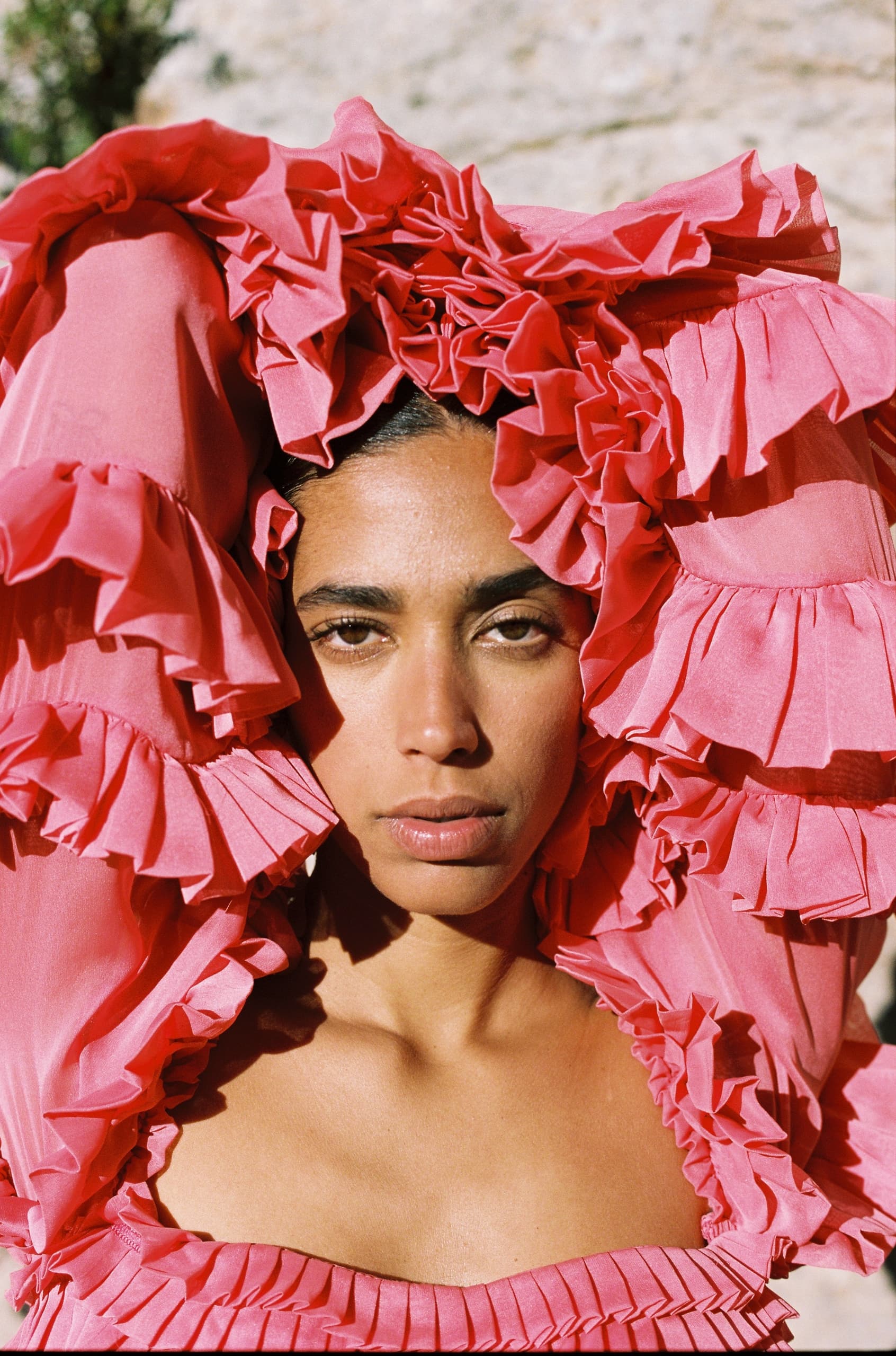 Woman in a vibrant pink ruffled outfit, striking pose, outdoor setting.