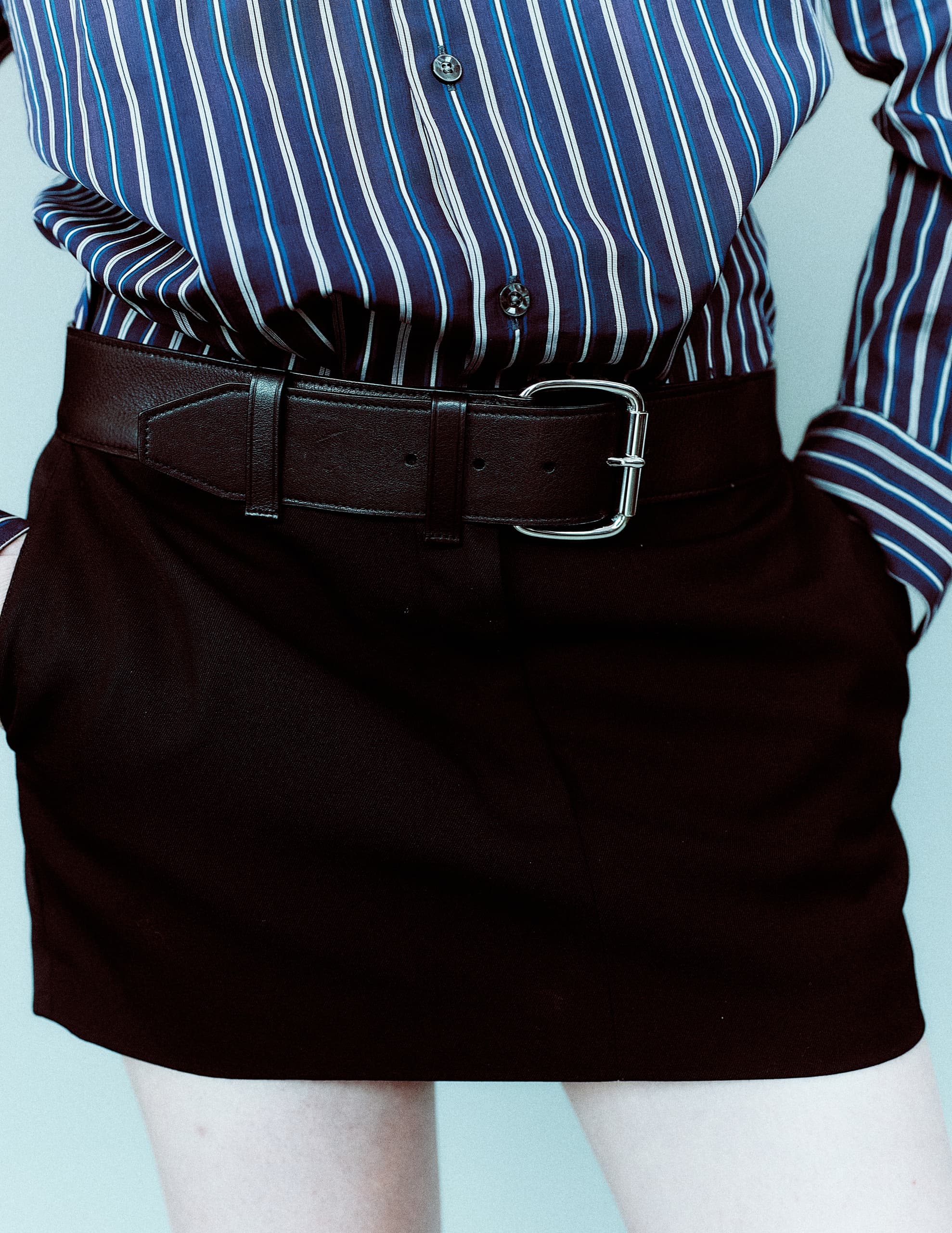 Person in striped shirt wearing a black skirt with a leather belt.