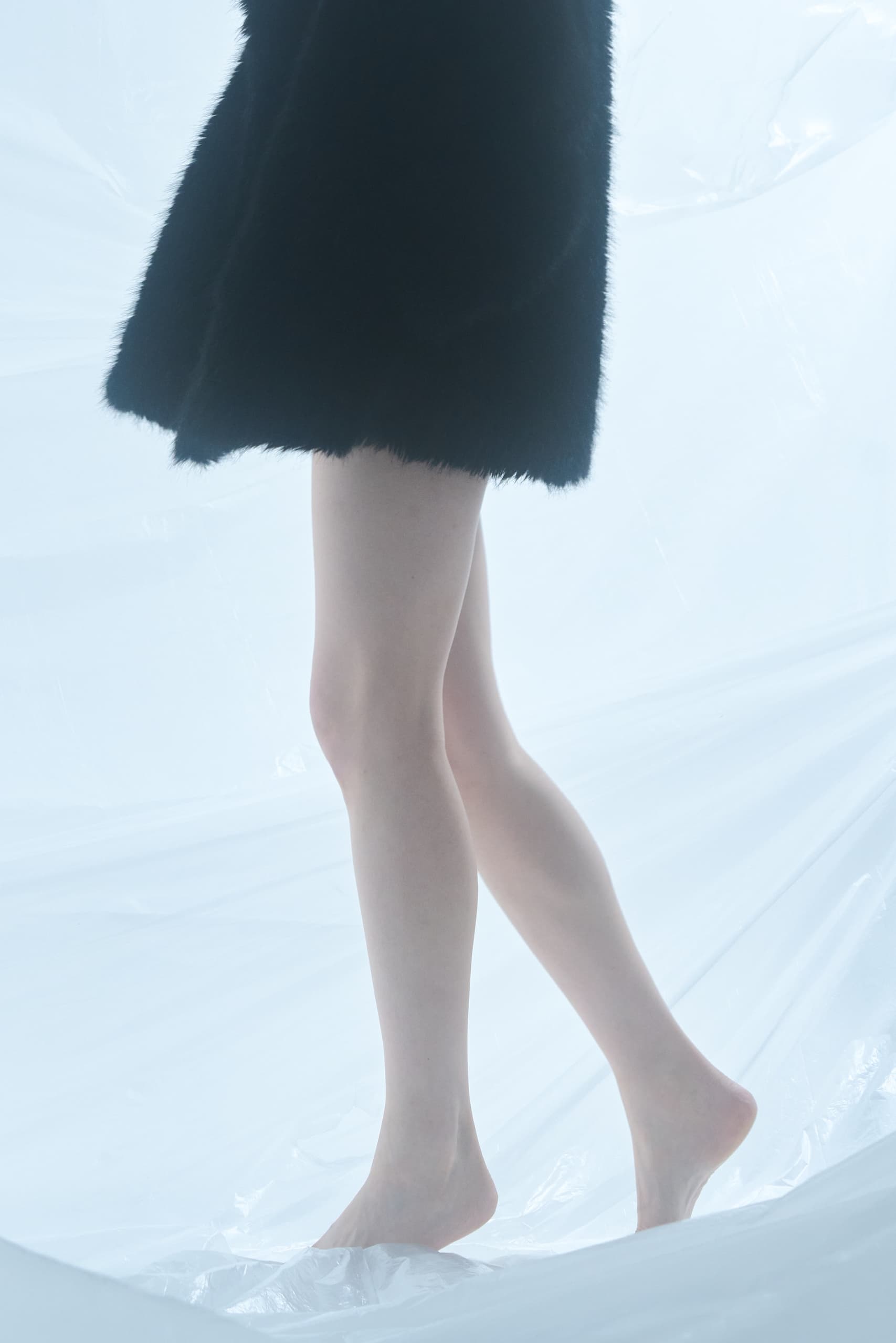 Bare legs in a black dress on a light background.