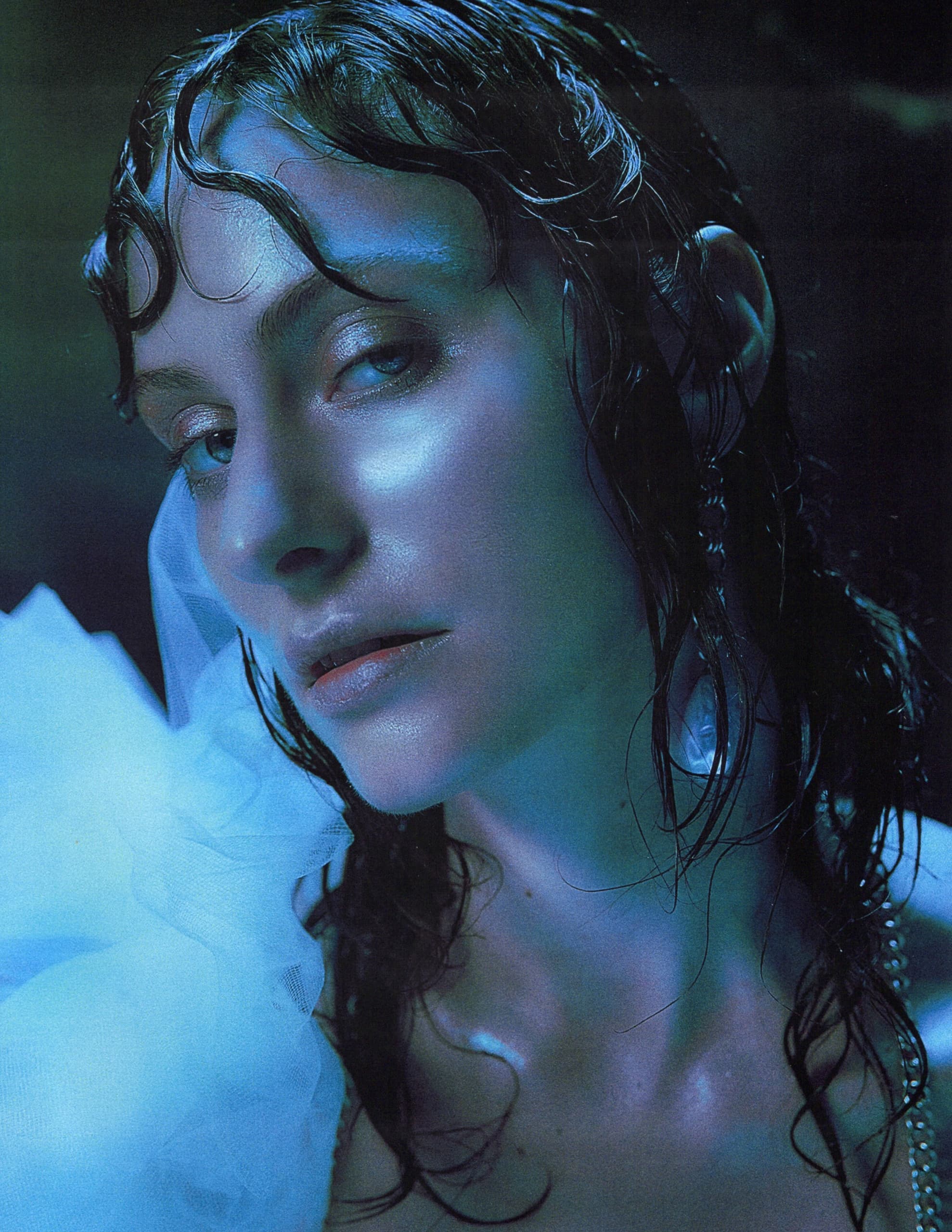 Mysterious woman with wet hair and blue lighting, wearing a sheer white fabric.
