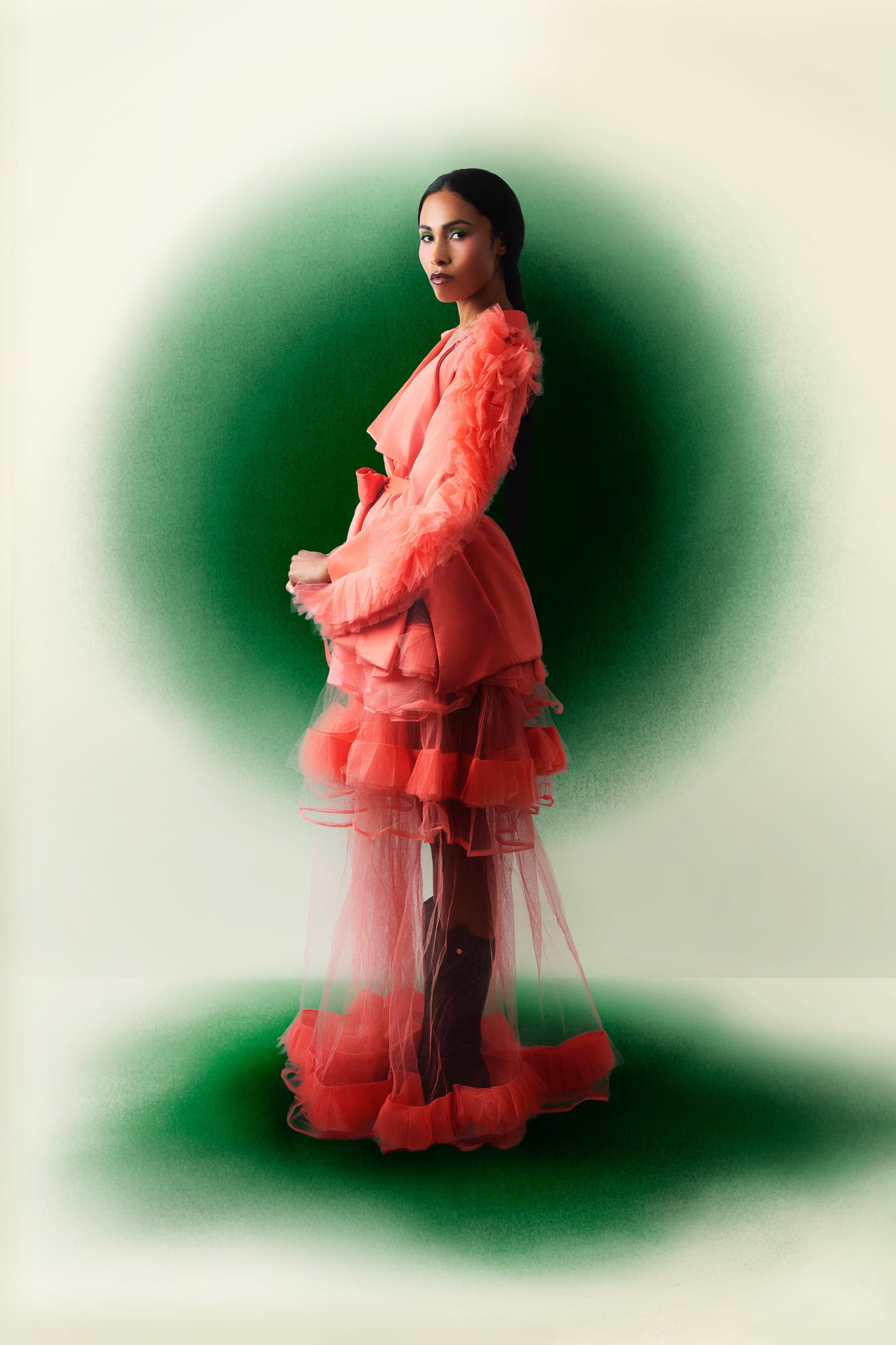 Woman in layered coral dress with a green gradient background.