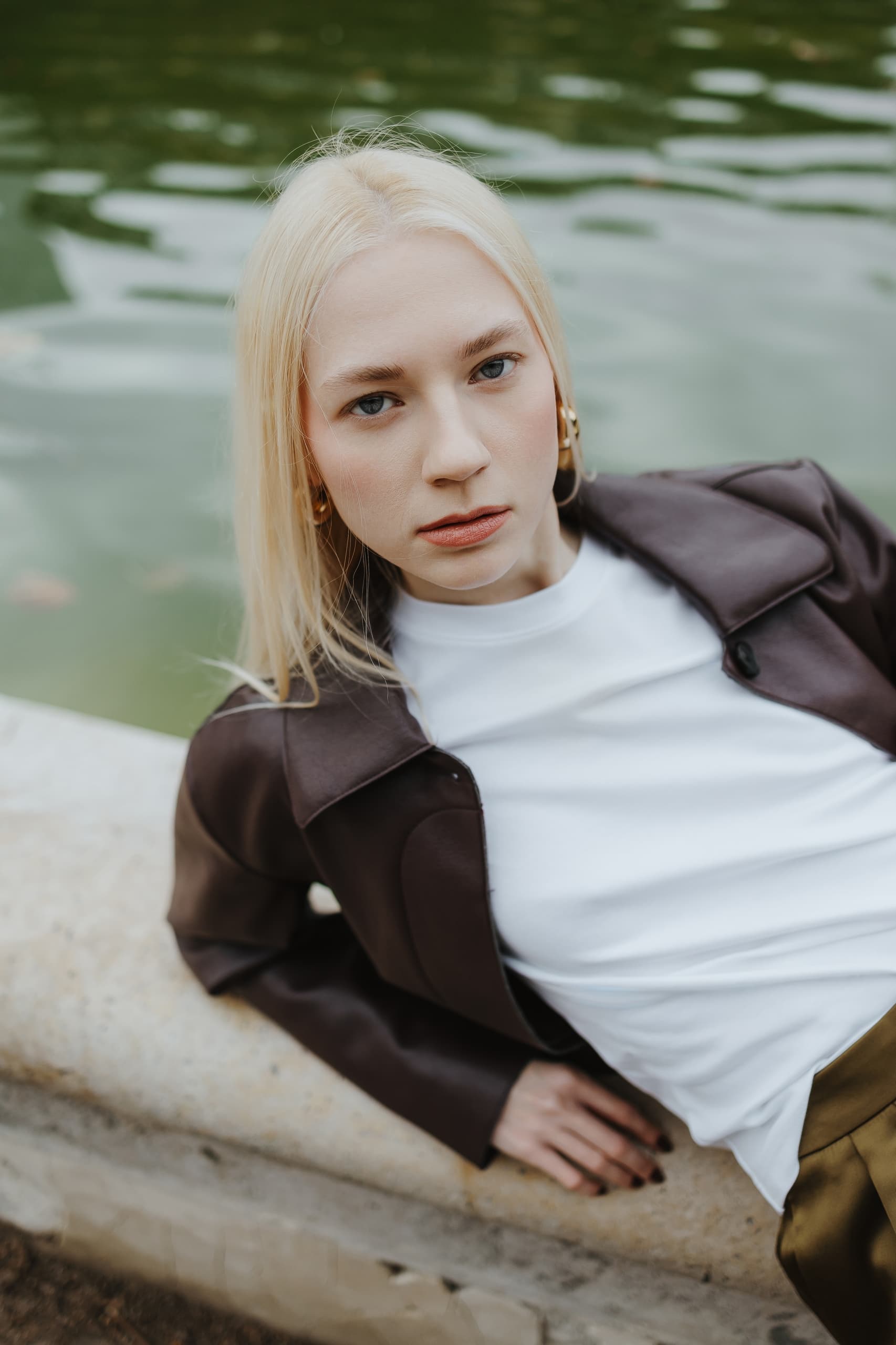 Stylish person in a leather jacket relaxing by a serene pond.