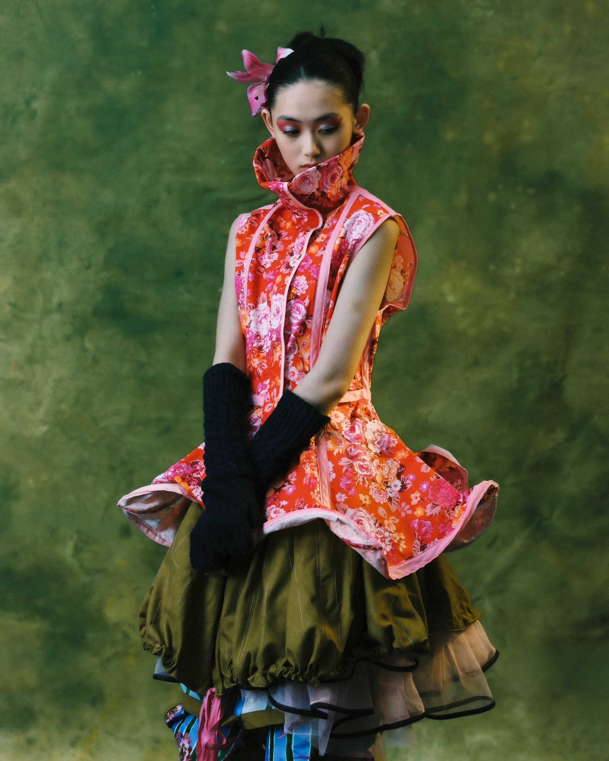 Fashionable woman in floral dress with high collar, layered skirt against green background.