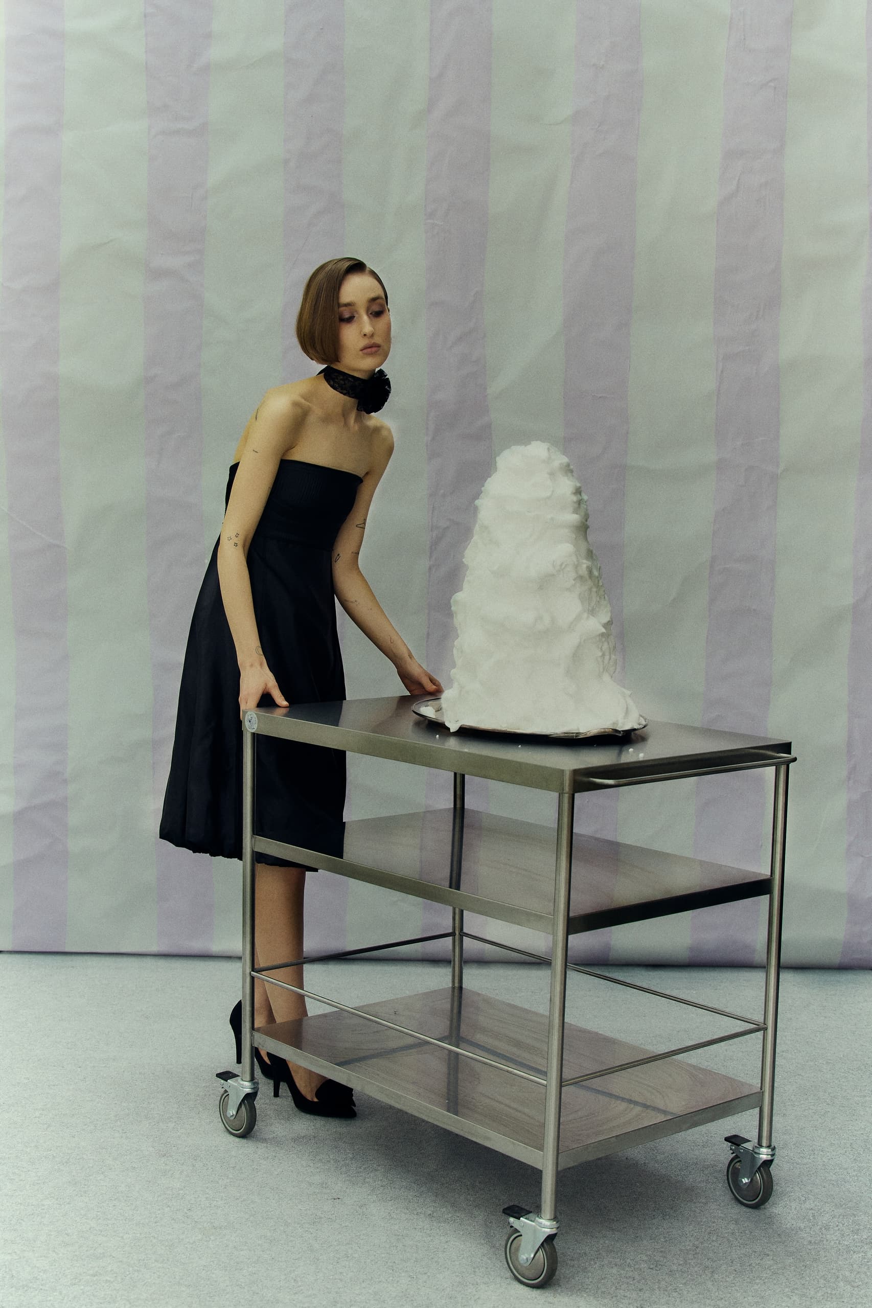 Elegant woman in black dress with a tiered sculpture on a rolling cart.