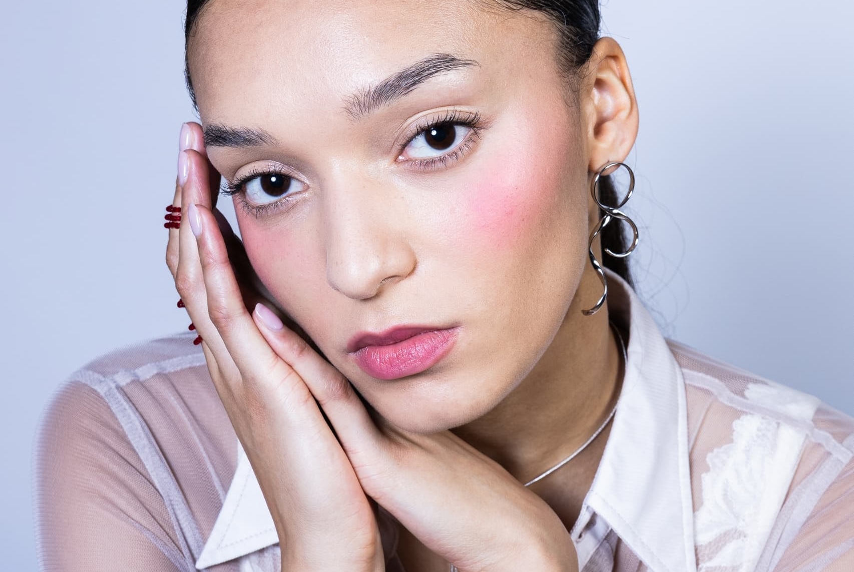 Close-up of woman with creative earrings, hand on face, and soft makeup look.