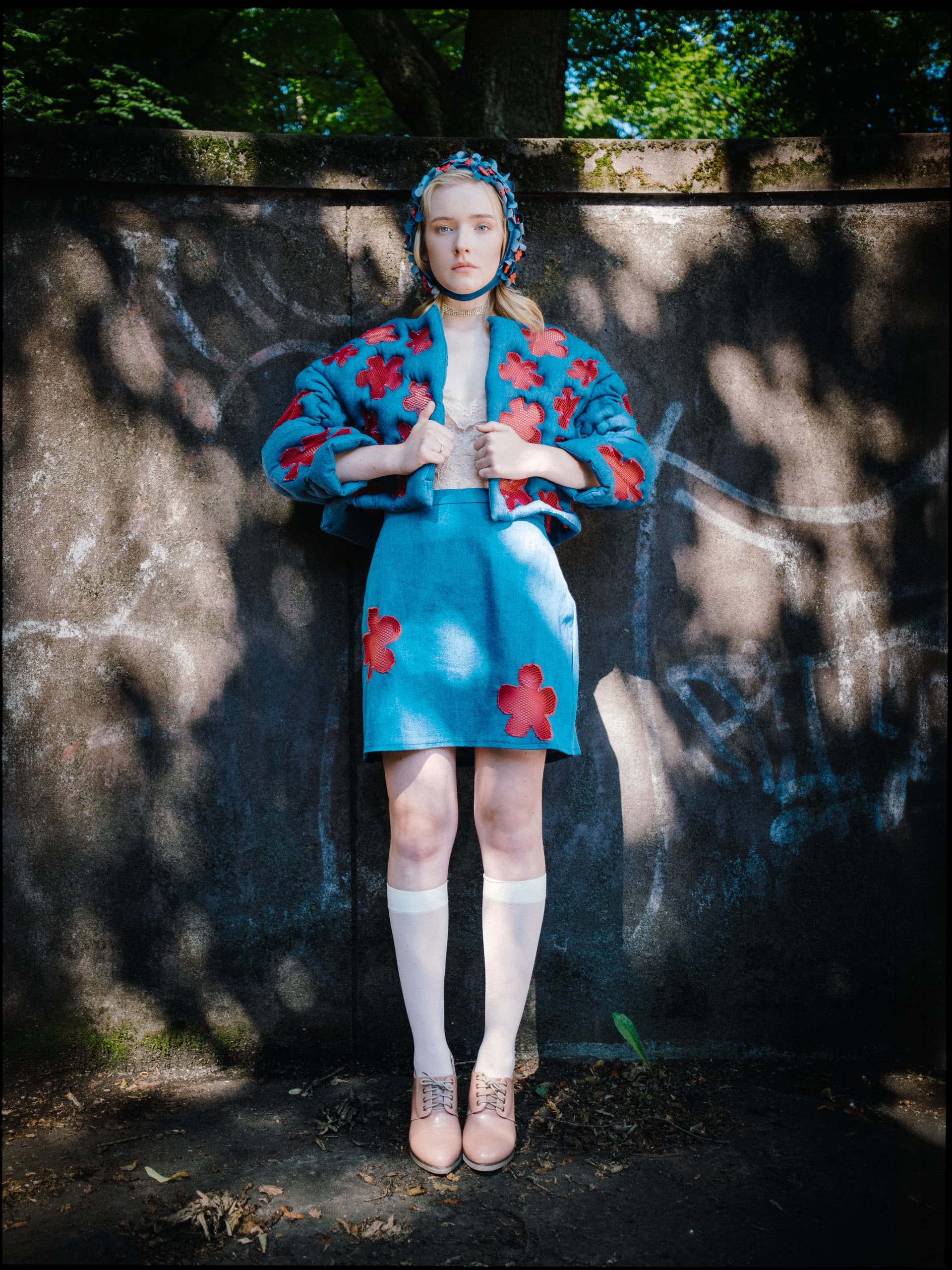 Fashionable person in blue floral outfit standing against a textured wall.