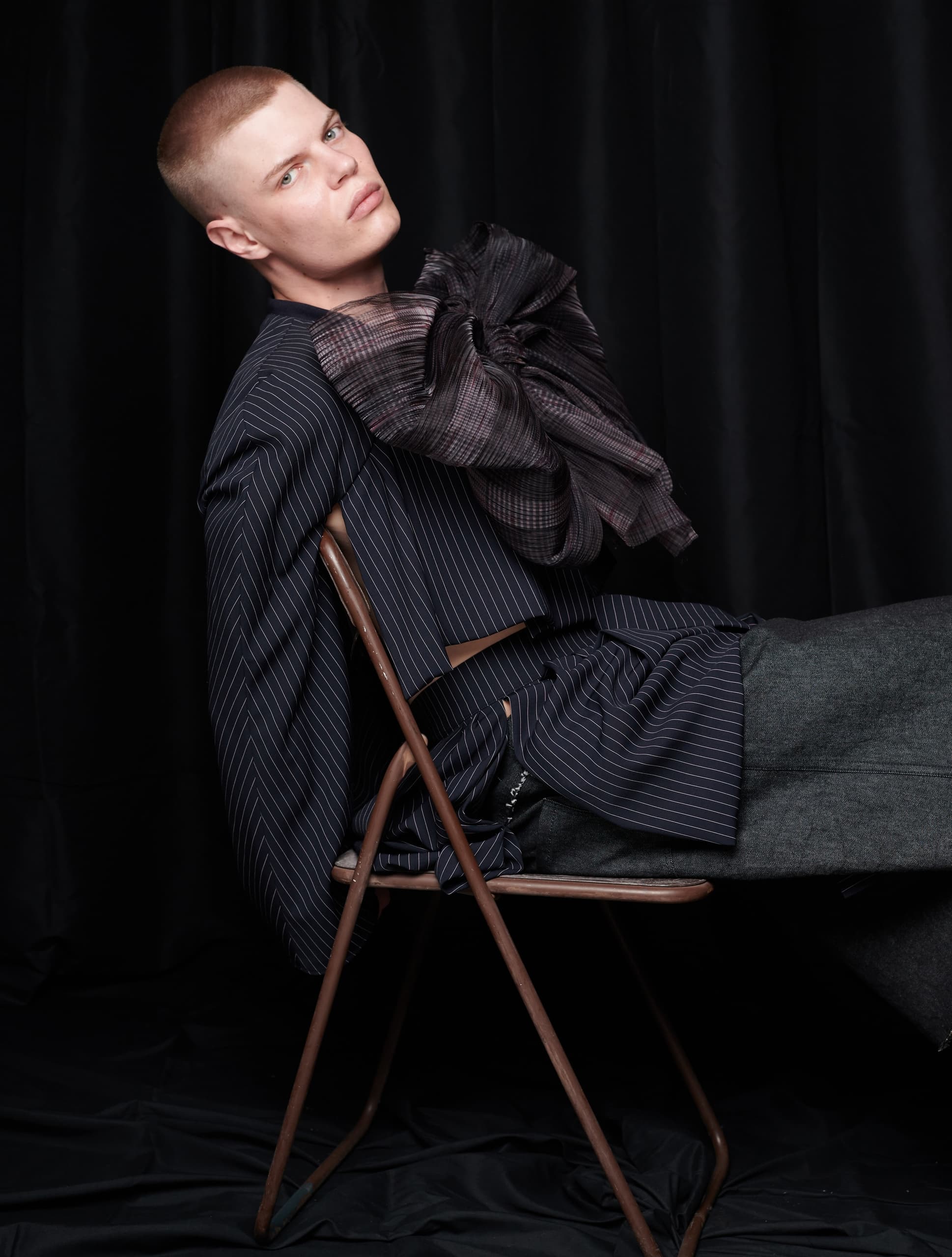 Person in stylish pinstripe suit sitting on chair against dark background.