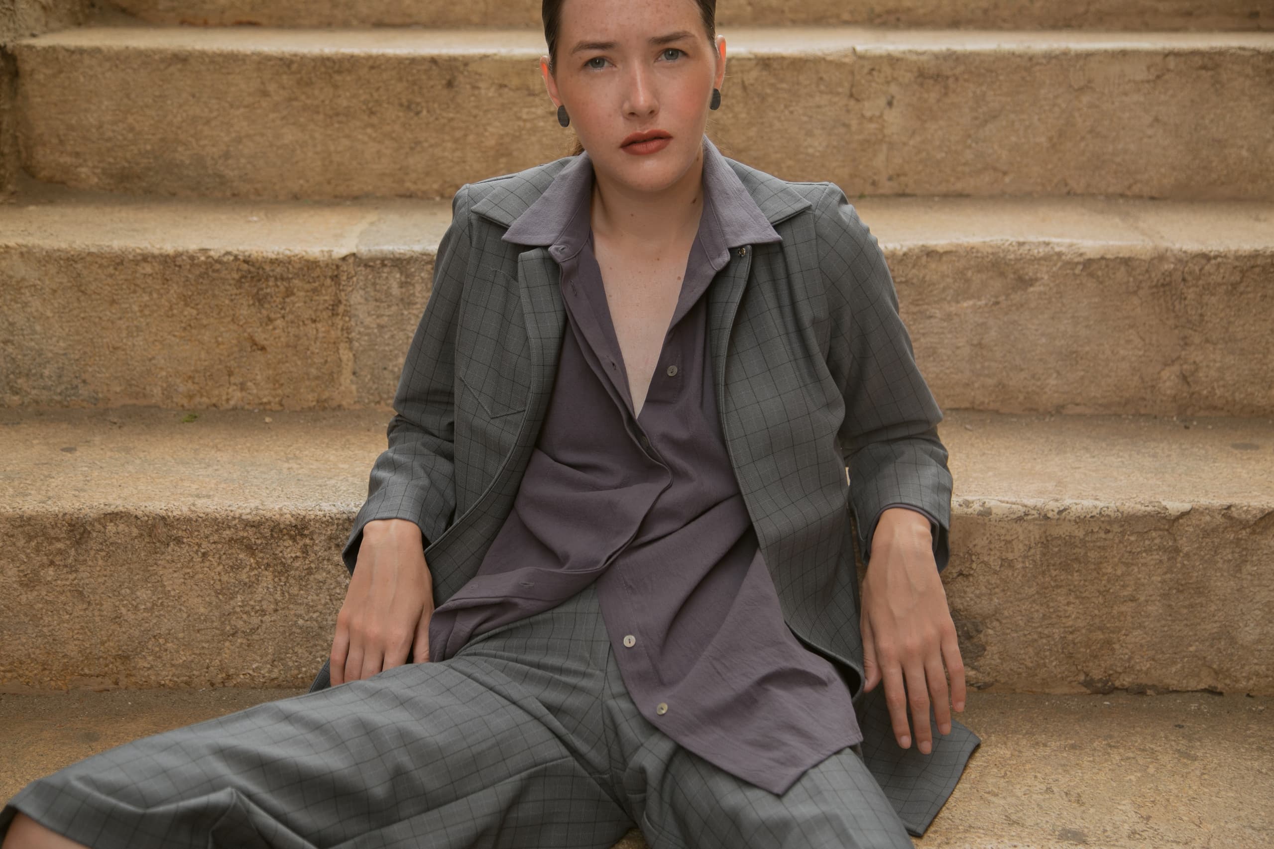 Person in gray plaid suit sitting on stone steps, casual yet stylish.