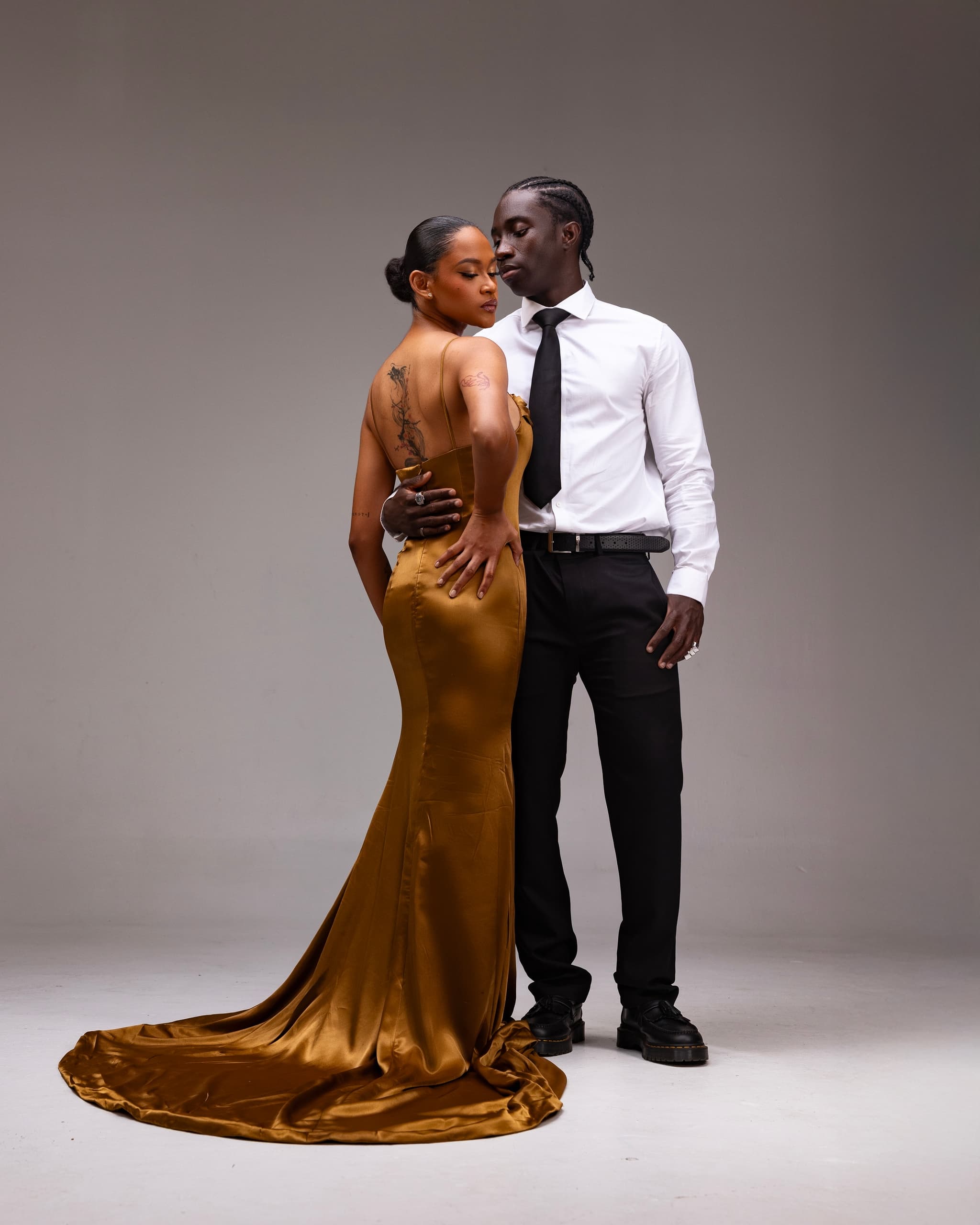 Elegant couple in formal attire, posing intimately against a plain background.