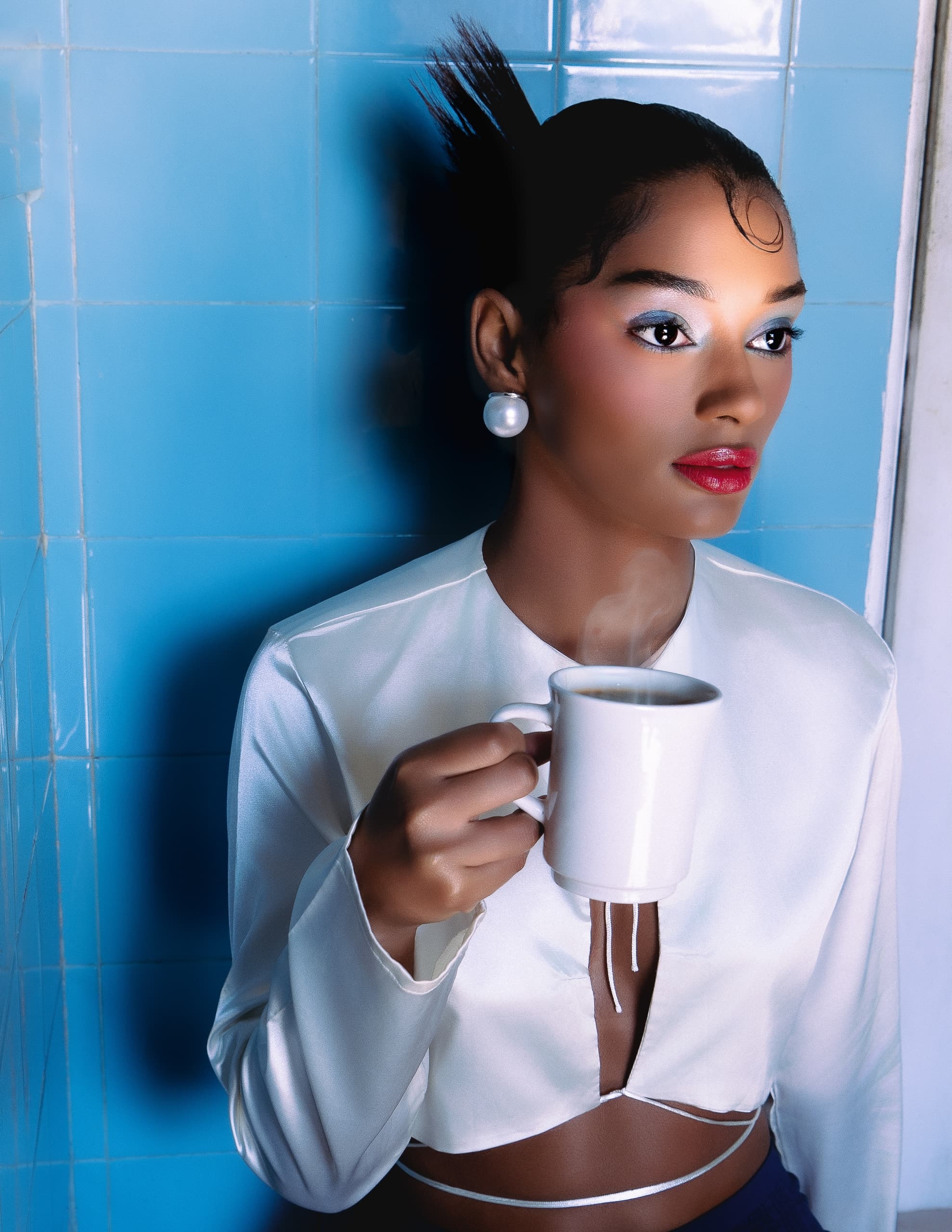 Woman in white blouse holding coffee cup against blue tiled wall.
